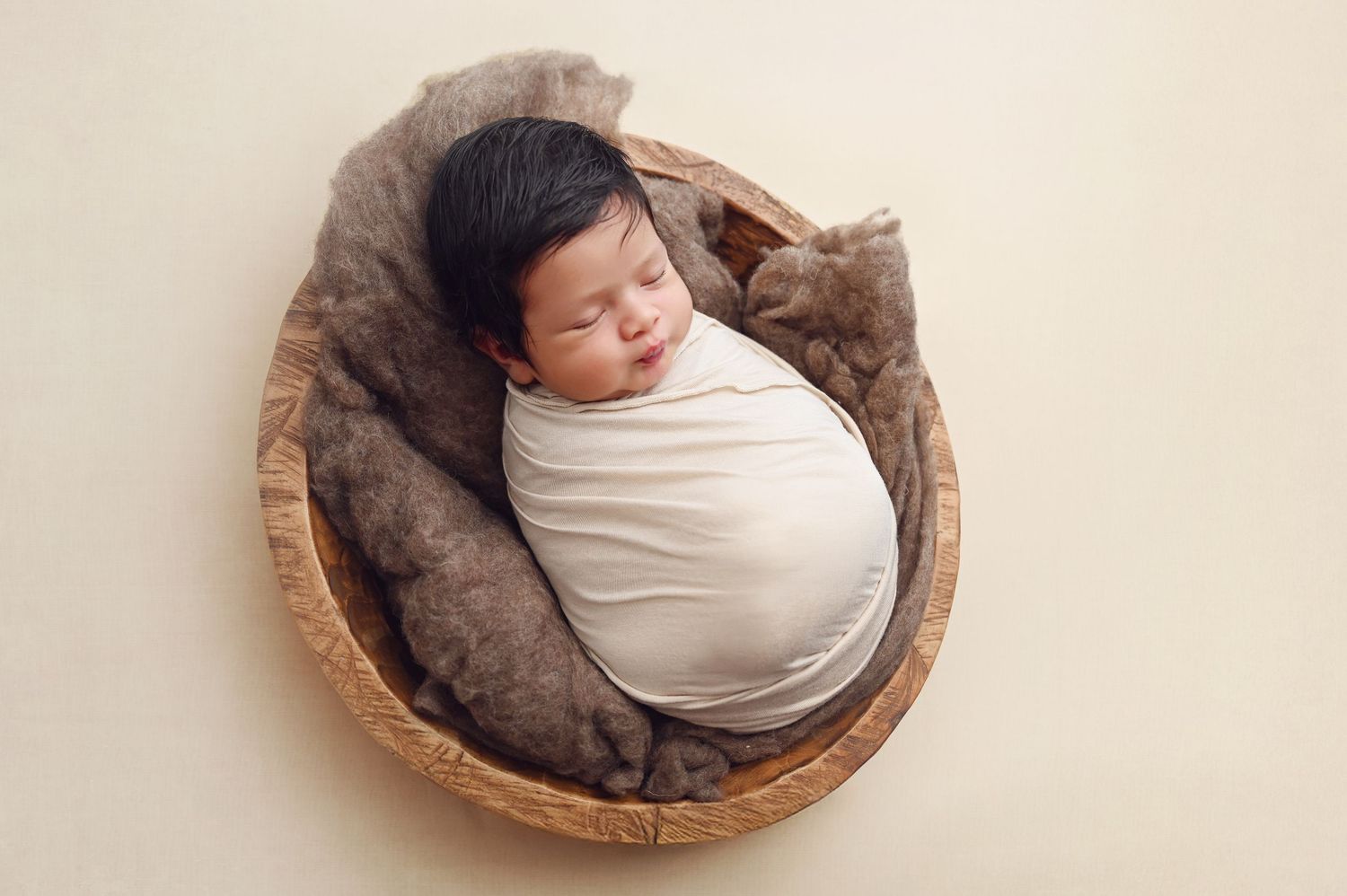 Sleeping newborn peacefully nestled in rustic wooden bowl with cream wrap. Hanford Newborn Photographer