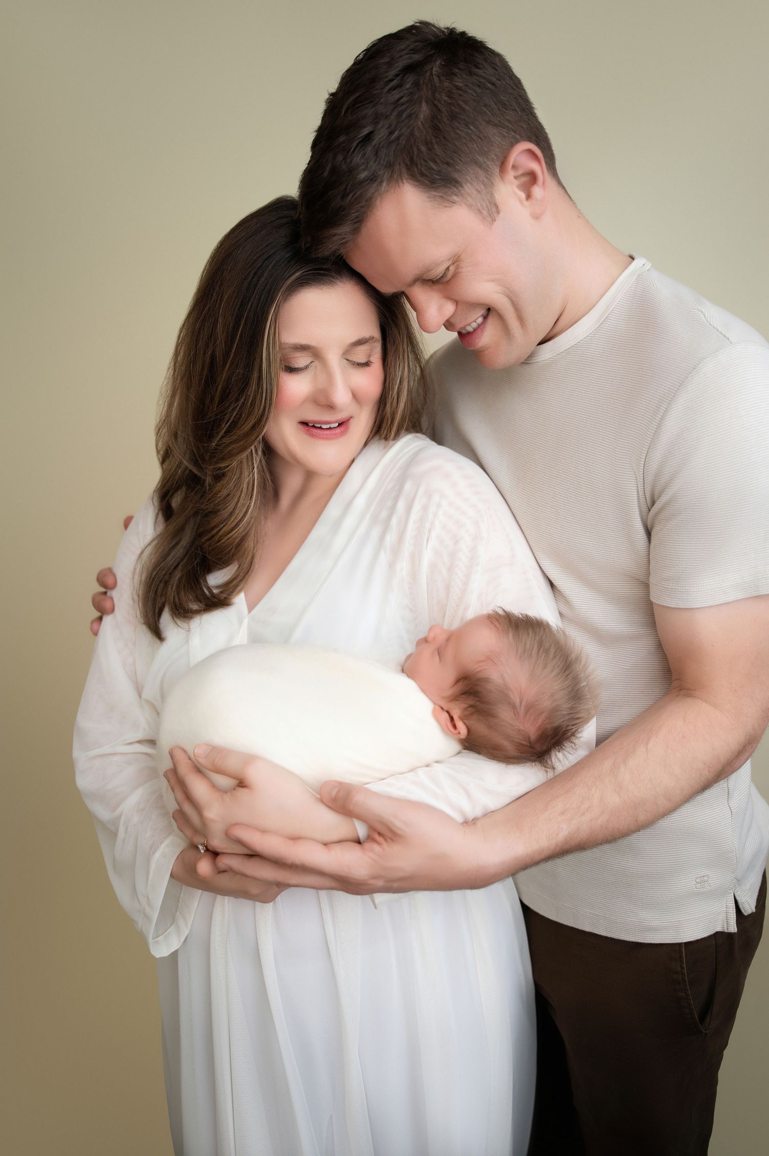 Intimate maternity photo series showing couple in white clothing embracing and looking down lovingly.