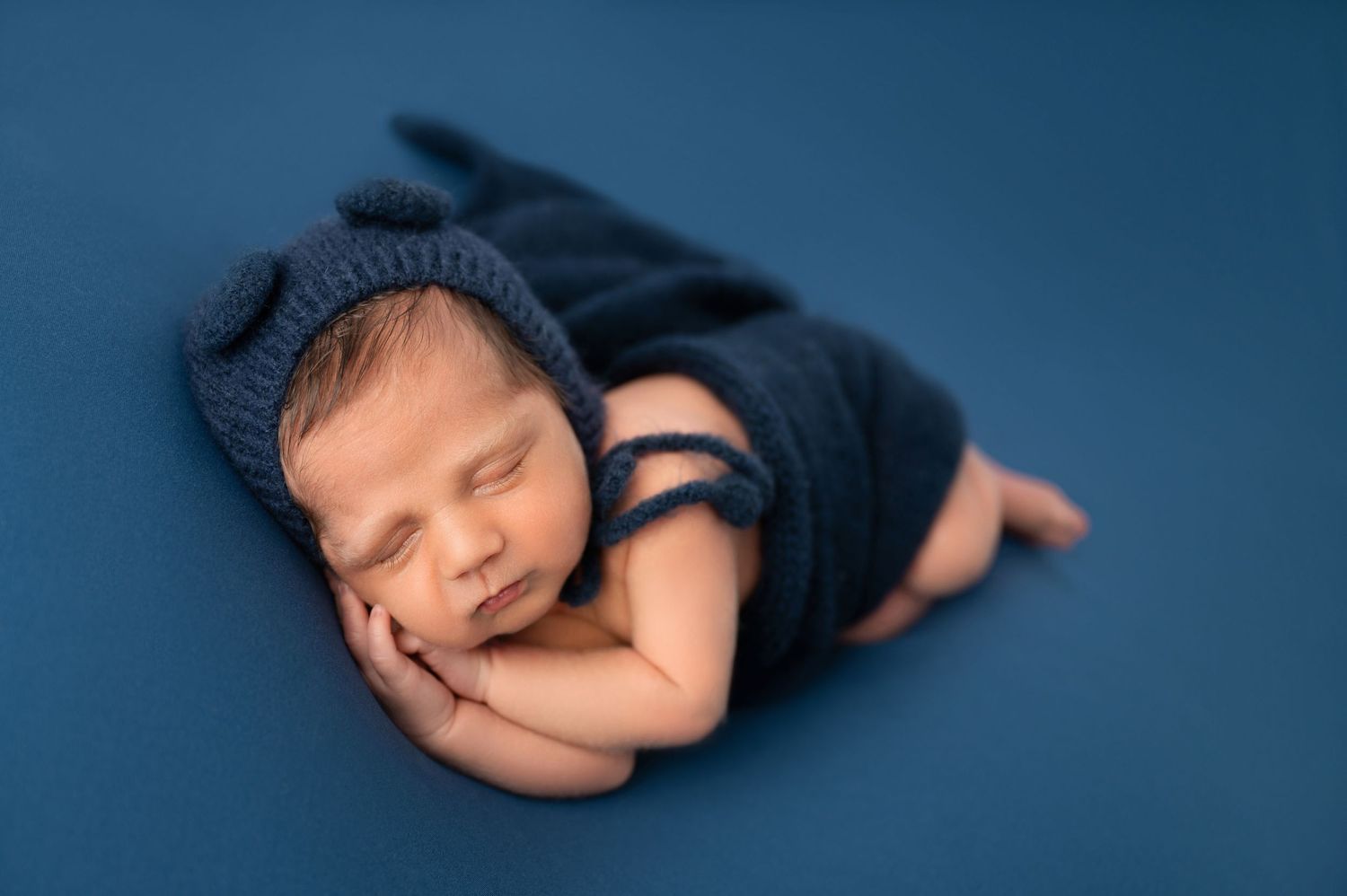 Peaceful newborn baby sleeping in navy wrap on blue background.