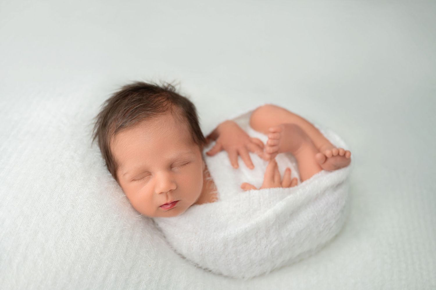 Sleeping newborn wrapped in white blanket during professional studio photography.