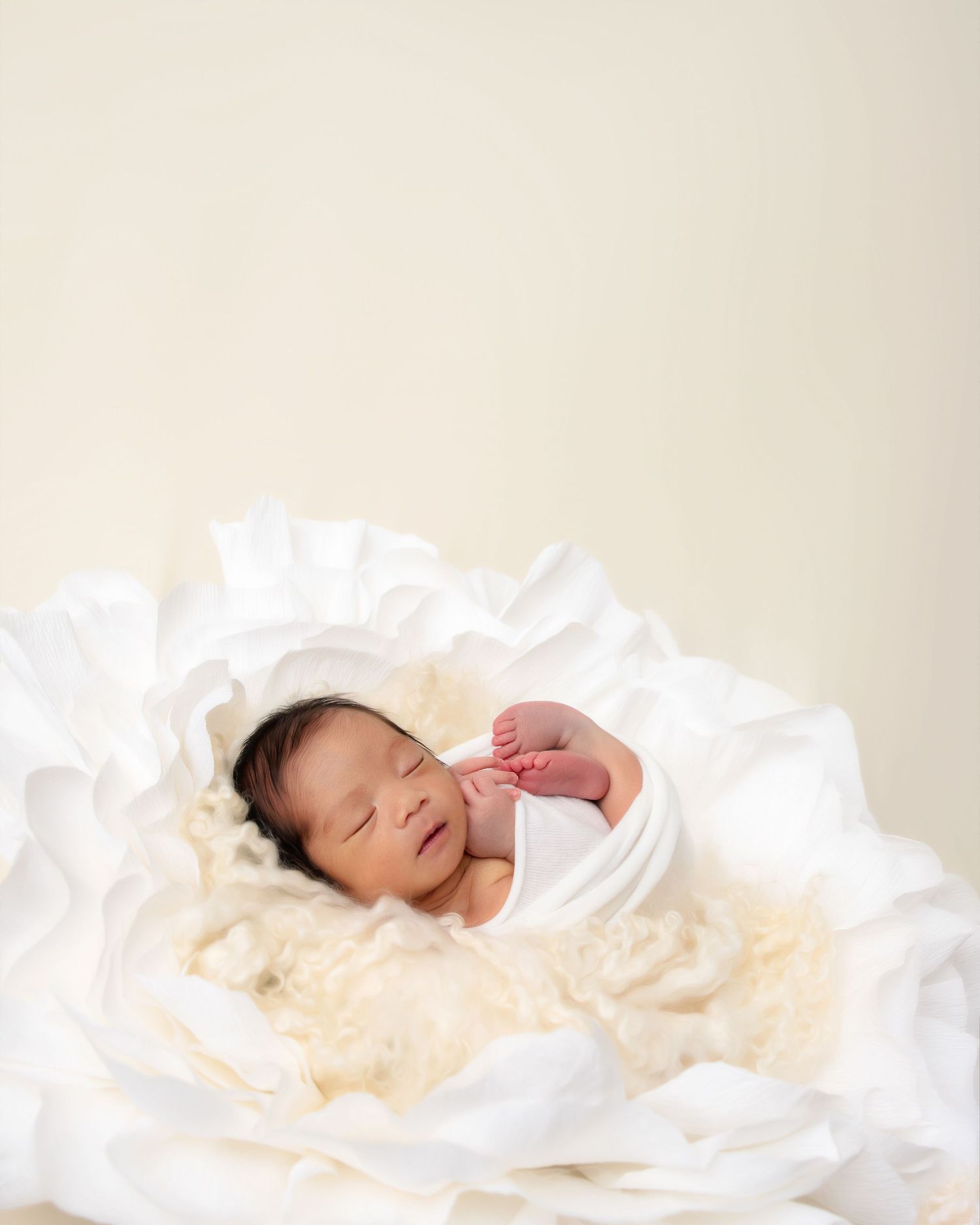 Peaceful sleeping newborn on soft cream-colored fabric with white accents.