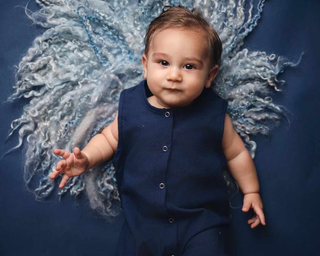 Baby in navy outfit photographed on white textured fabric against deep blue background.