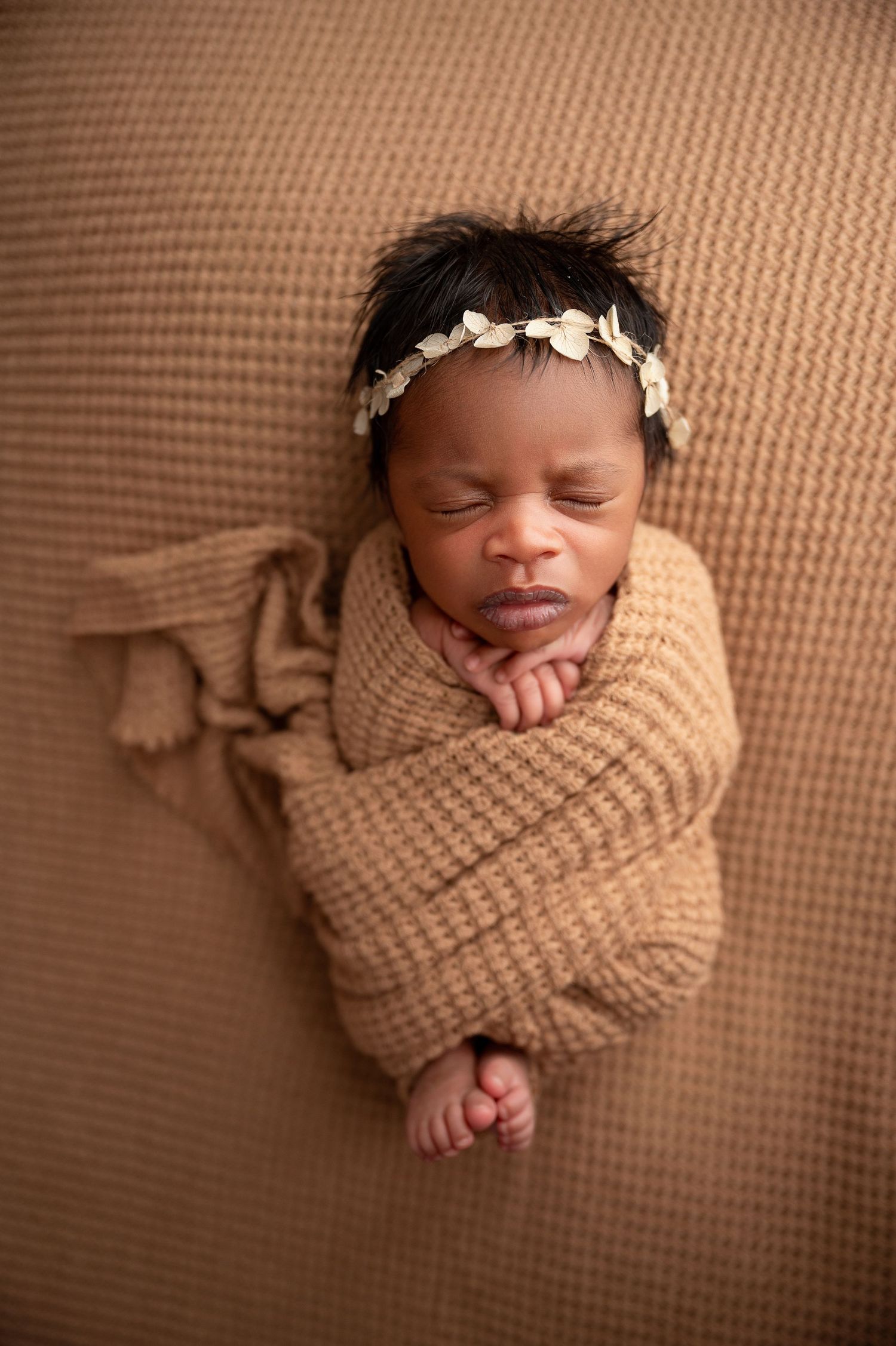 Newborn photography series with baby wrapped in tan knit blanket wearing delicate headband.
