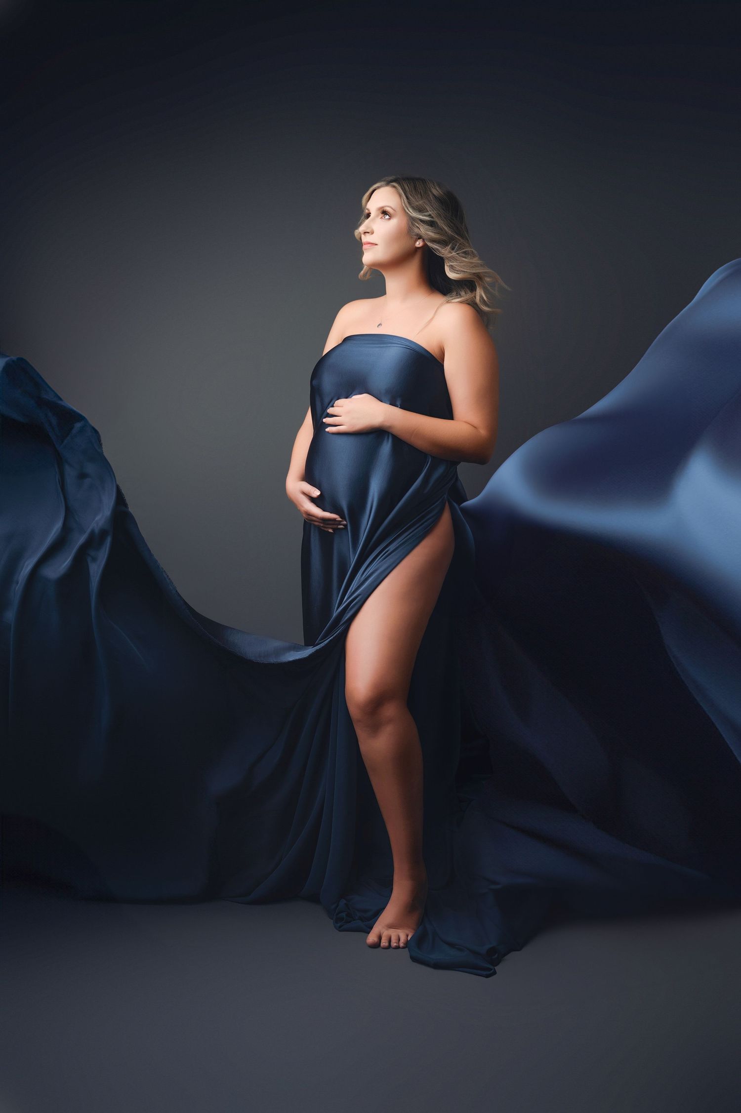 Elegant maternity photos with navy blue fabric flowing dramatically in studio setting.
