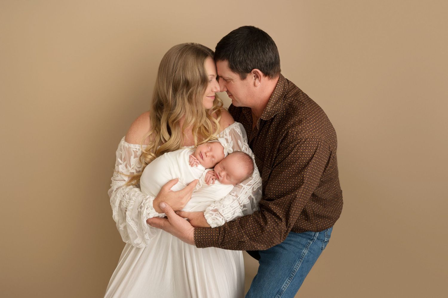 Tender newborn photography session with parents holding baby in soft beige studio setting.