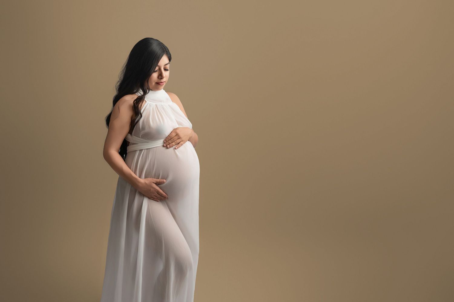 Silhouetted maternity photos show a pregnant woman in a flowing white dress against a neutral background. Hanford Maternity Photographer
