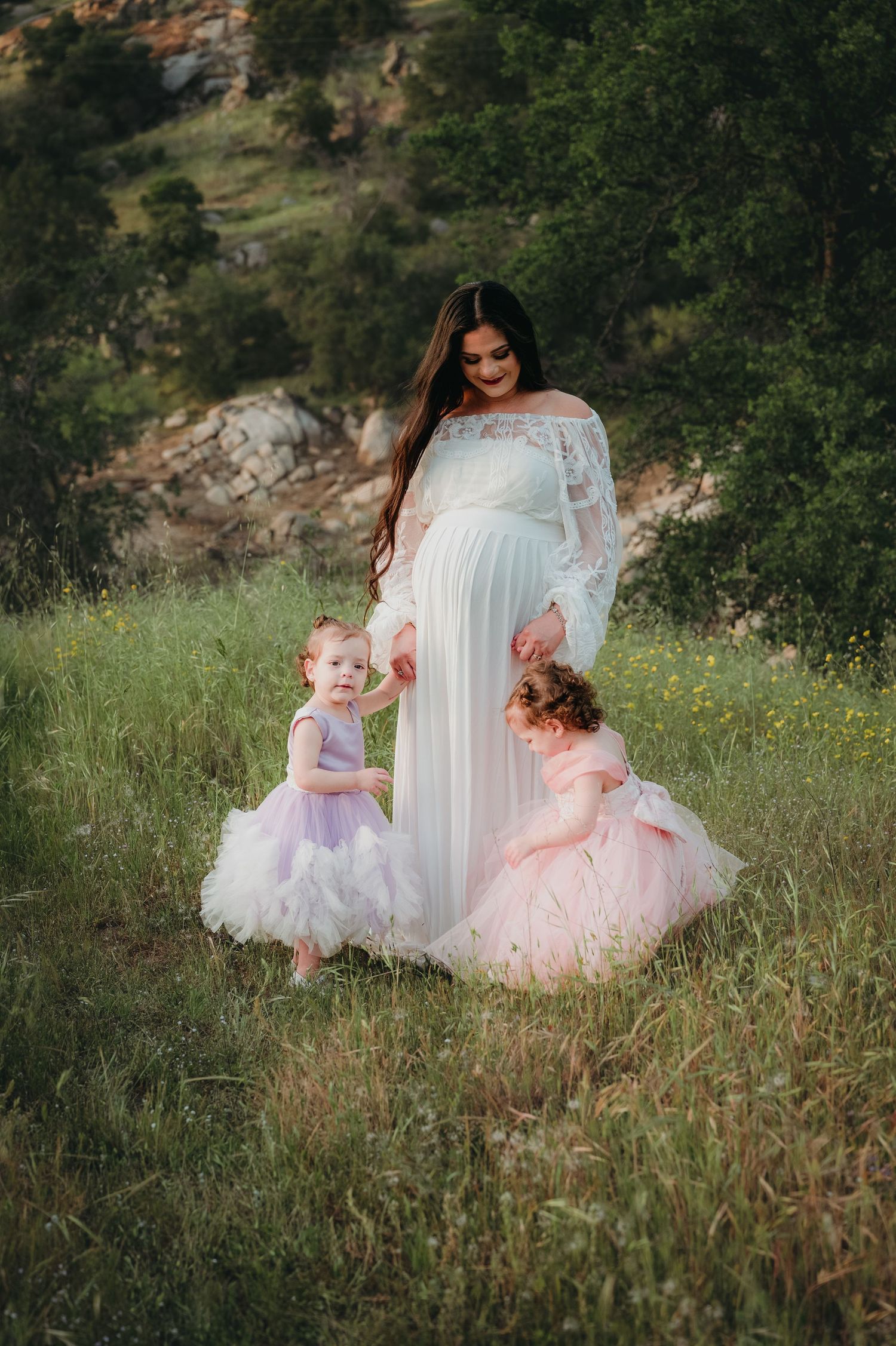Three figures in ethereal dresses stand together in a wildflower meadow. Fresno Family Photography