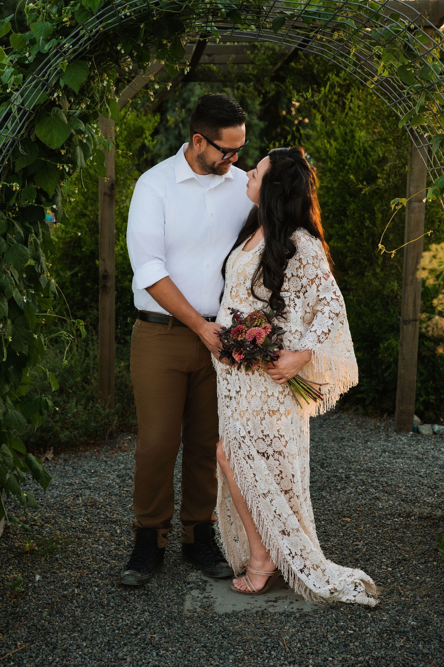 A romantic couple shares tender moments in a garden setting with greenery and gravel paths.