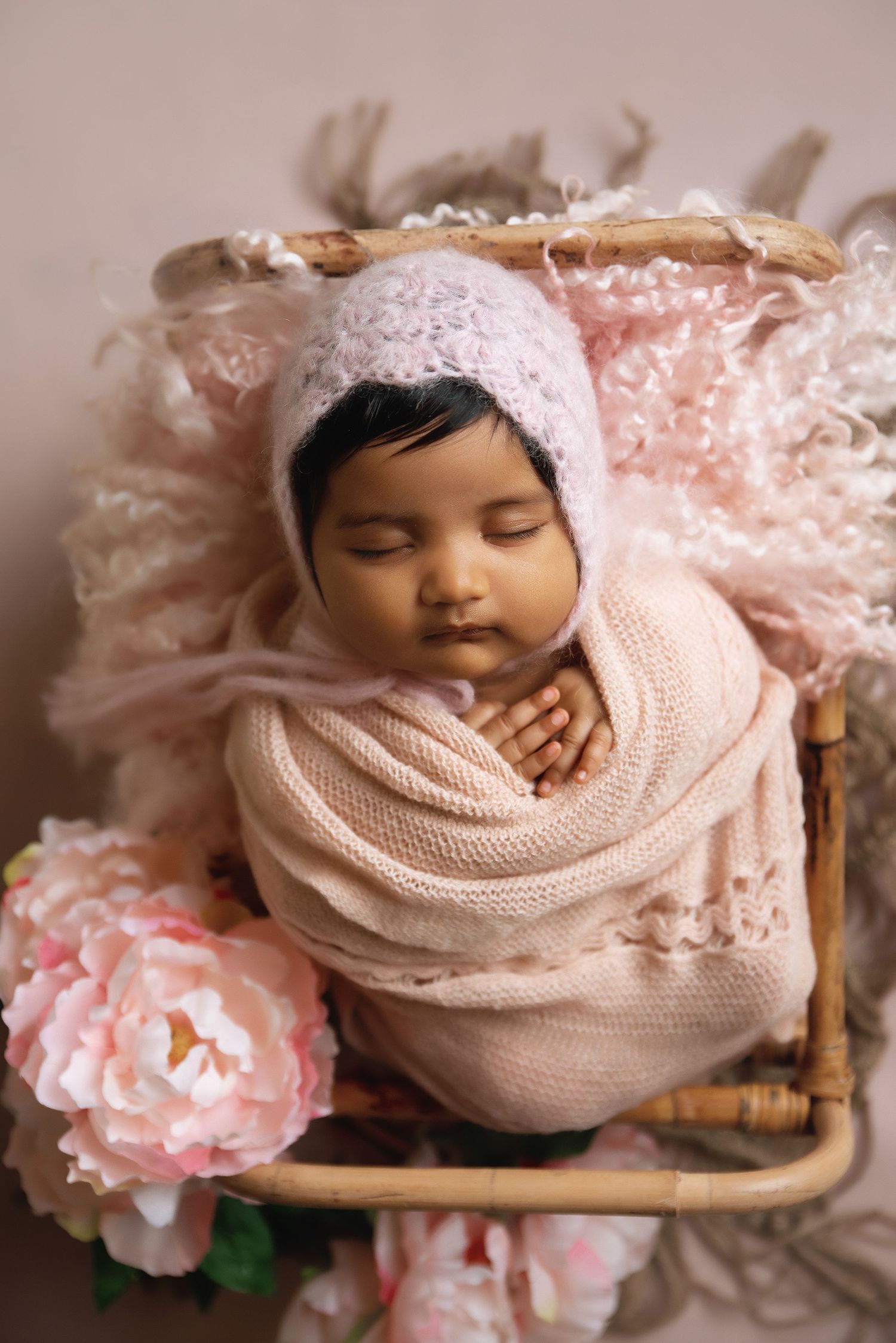 Newborn portrait in pink knit wrap with floral decorations.