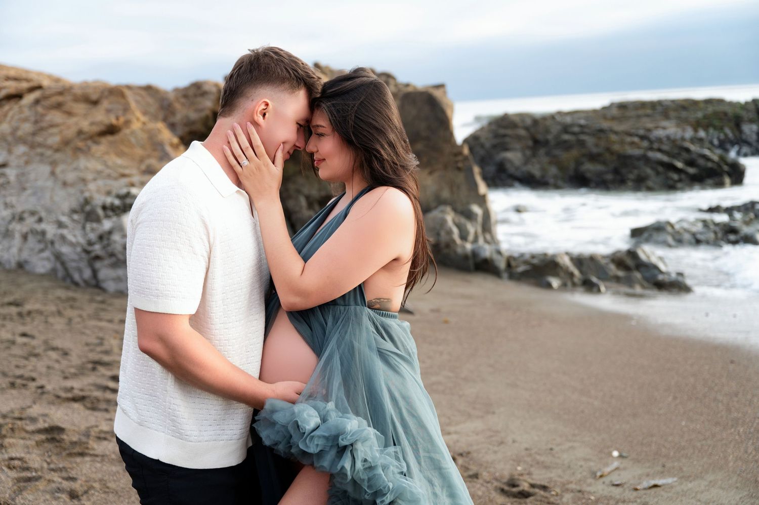 Tender moment captured during beach maternity session with teal dress.