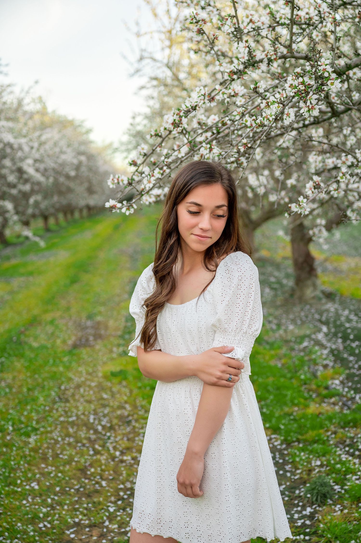 A white lace dress portrait amid blooming spring trees in an orchard setting.