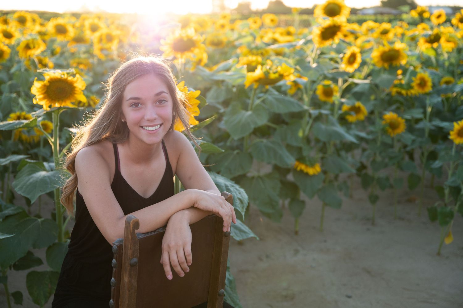 A black dress stands out against a vibrant sunflower field at golden hour.
