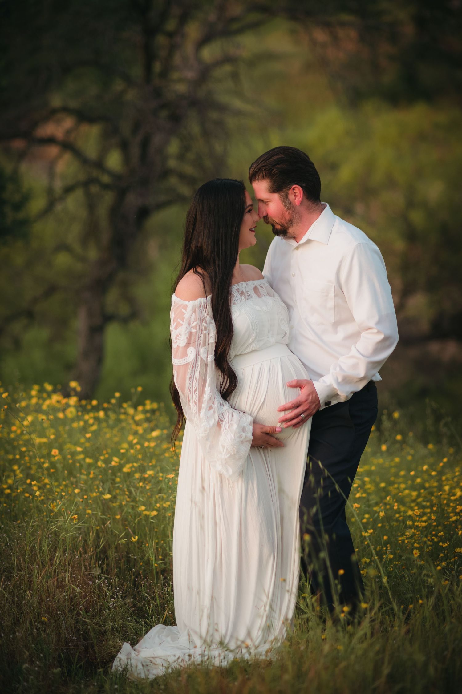 Romantic maternity portraits in white lace dress among wildflowers at golden hour.