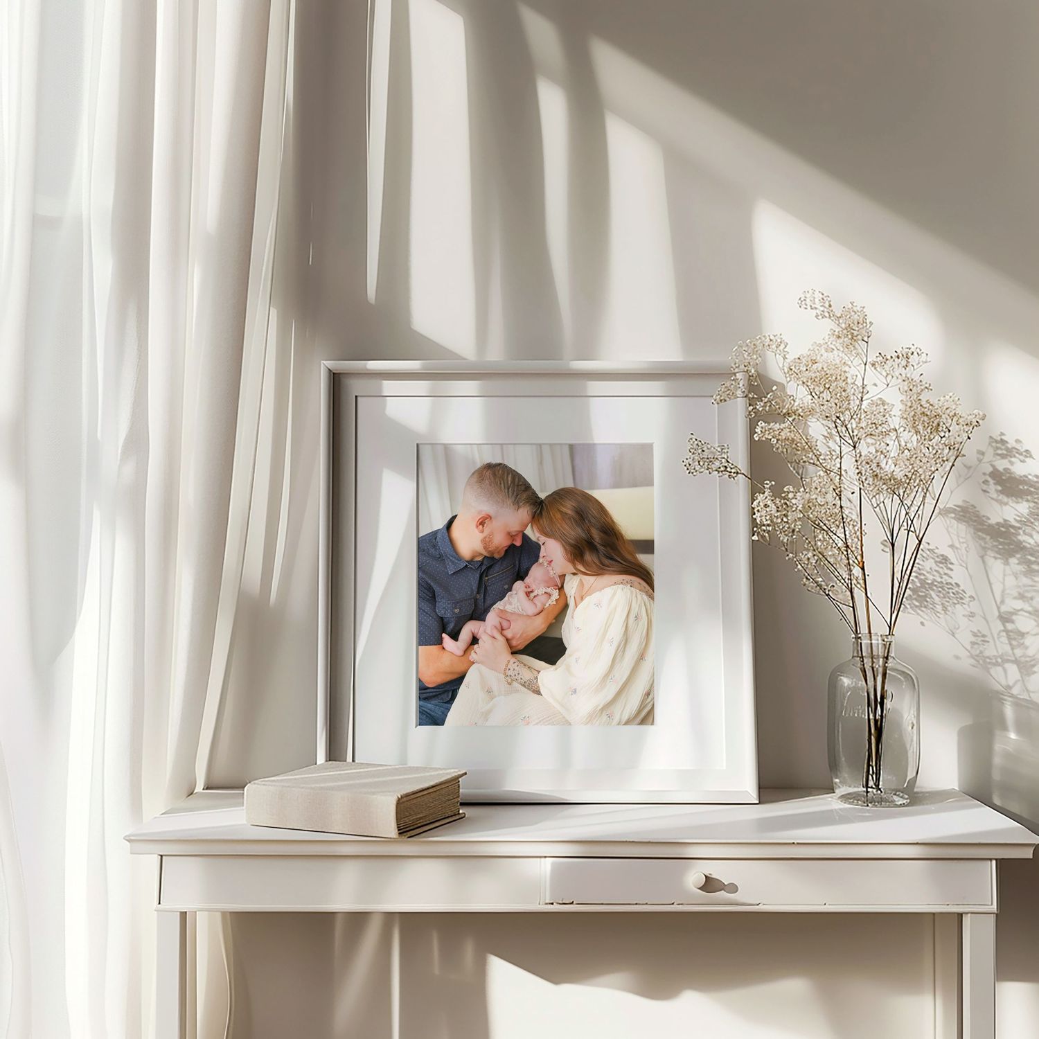 Clean white shelf display of framed family photos with dried flowers and natural light.