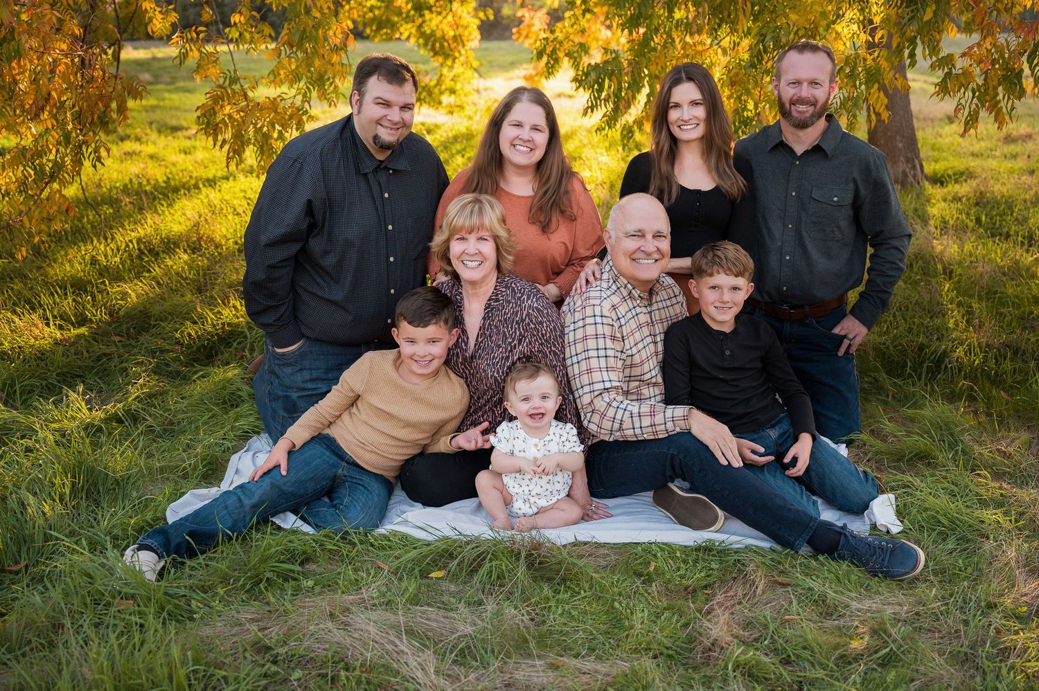 Extended family poses together on grass during fall outdoor photography session. Hanford Family Photographer