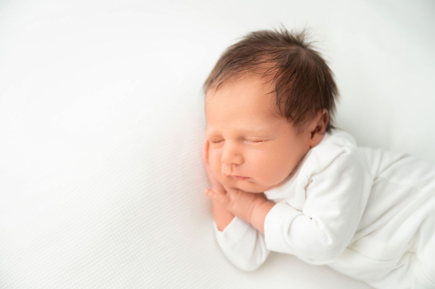Sweet newborn baby in white sleepwear sleeping on neutral background.