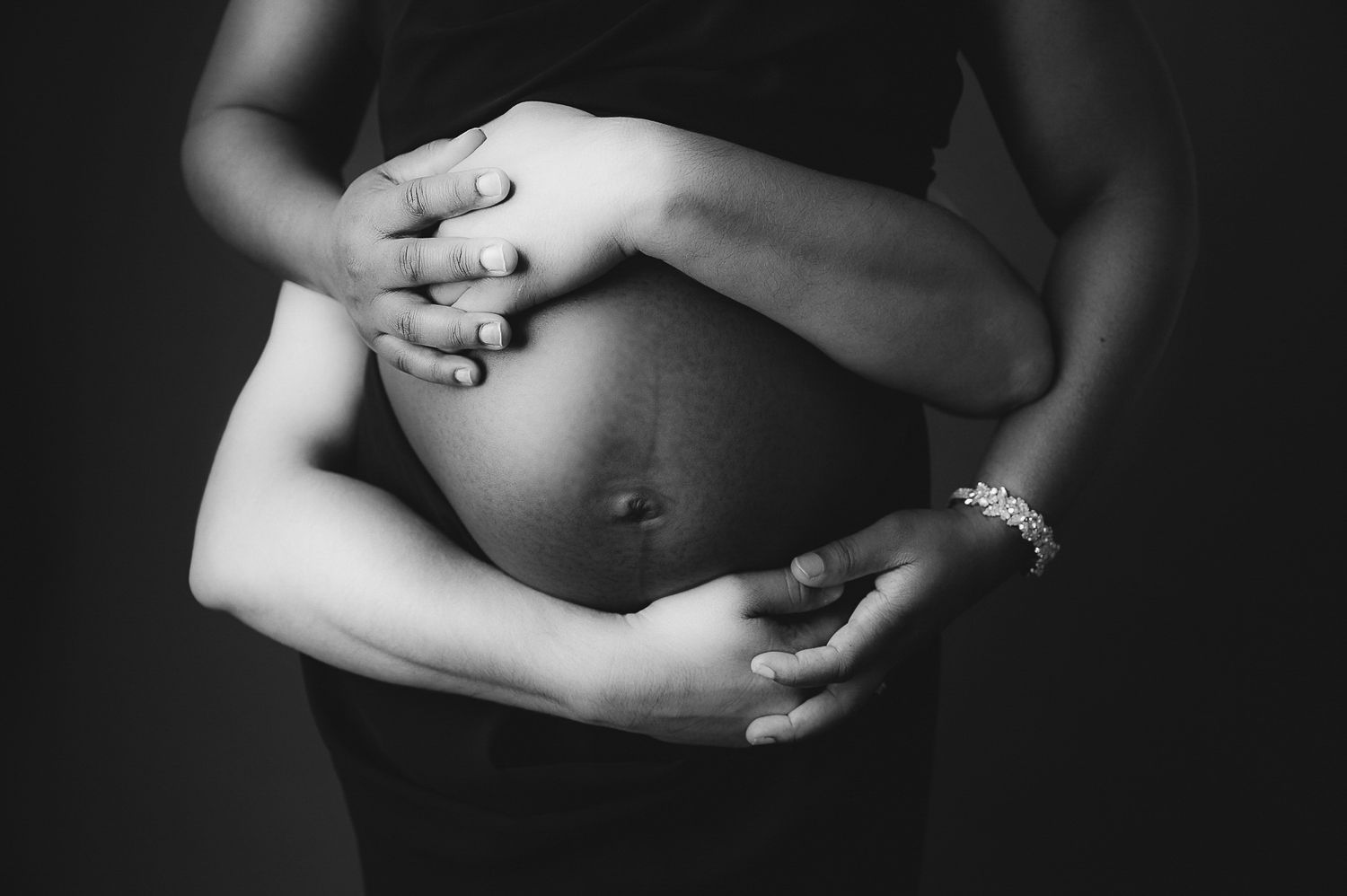 Artistic black and white maternity photo showing hands cradling a pregnant belly.