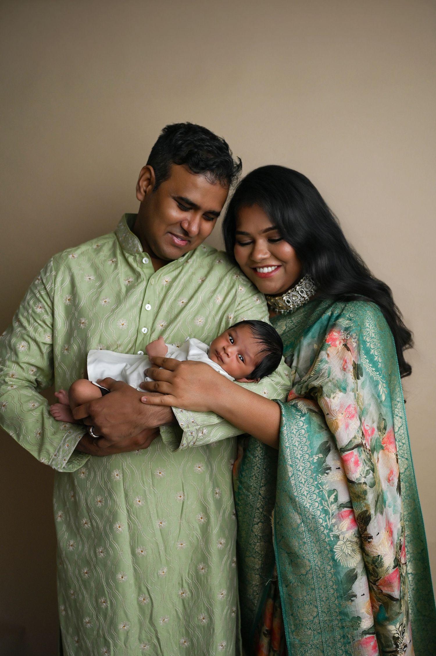 Family portrait series in traditional green and floral outfits holding their newborn with joy. Hanford Newborn Photographer