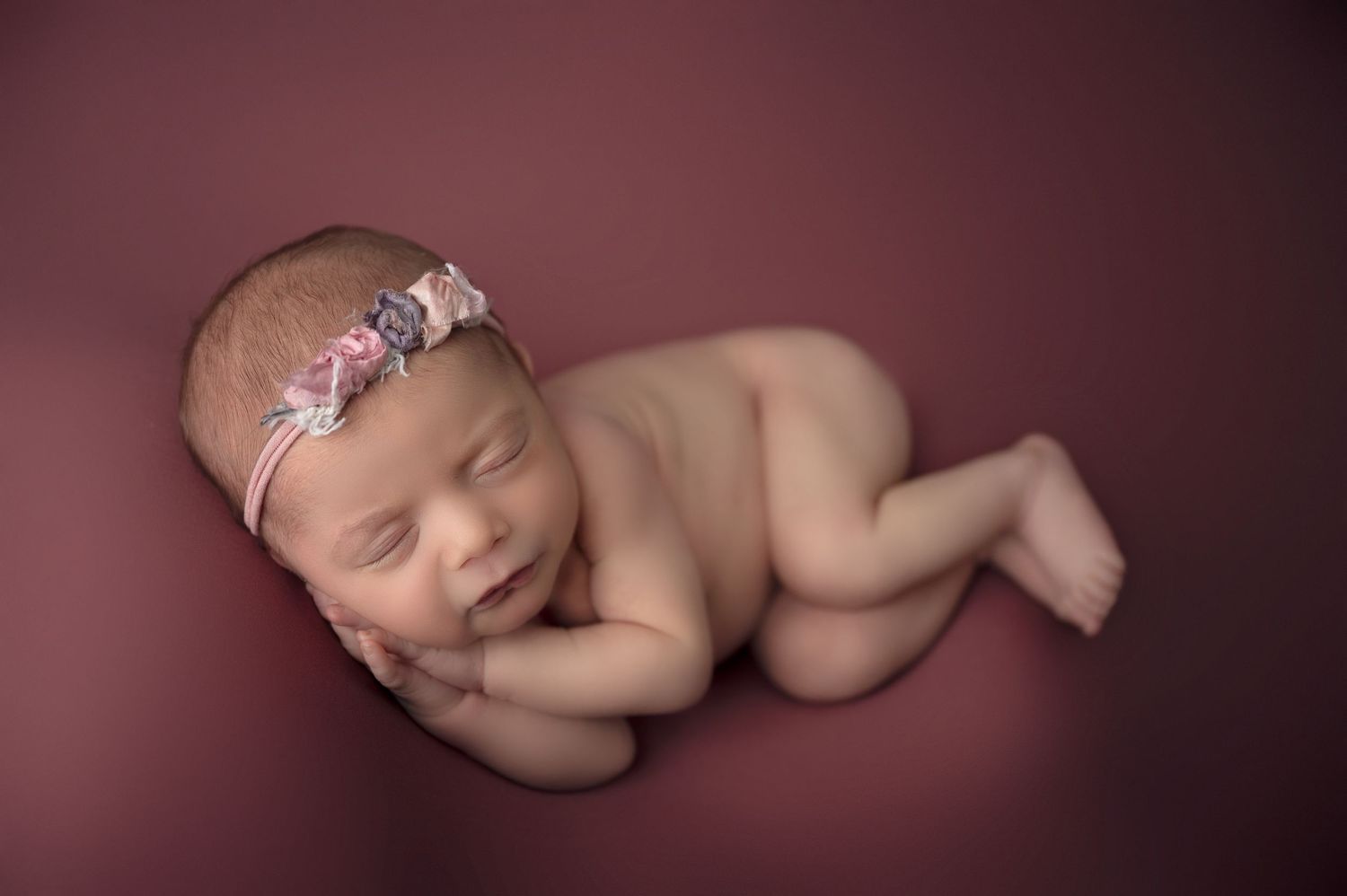 Artistic newborn portrait series against a deep burgundy background.