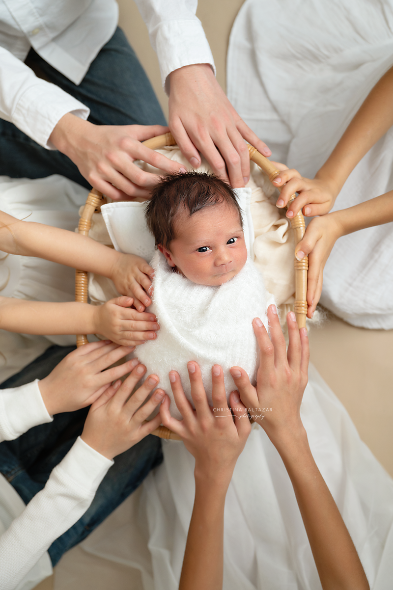 Multiple hands forming a circle around newborn baby in white clothing.
