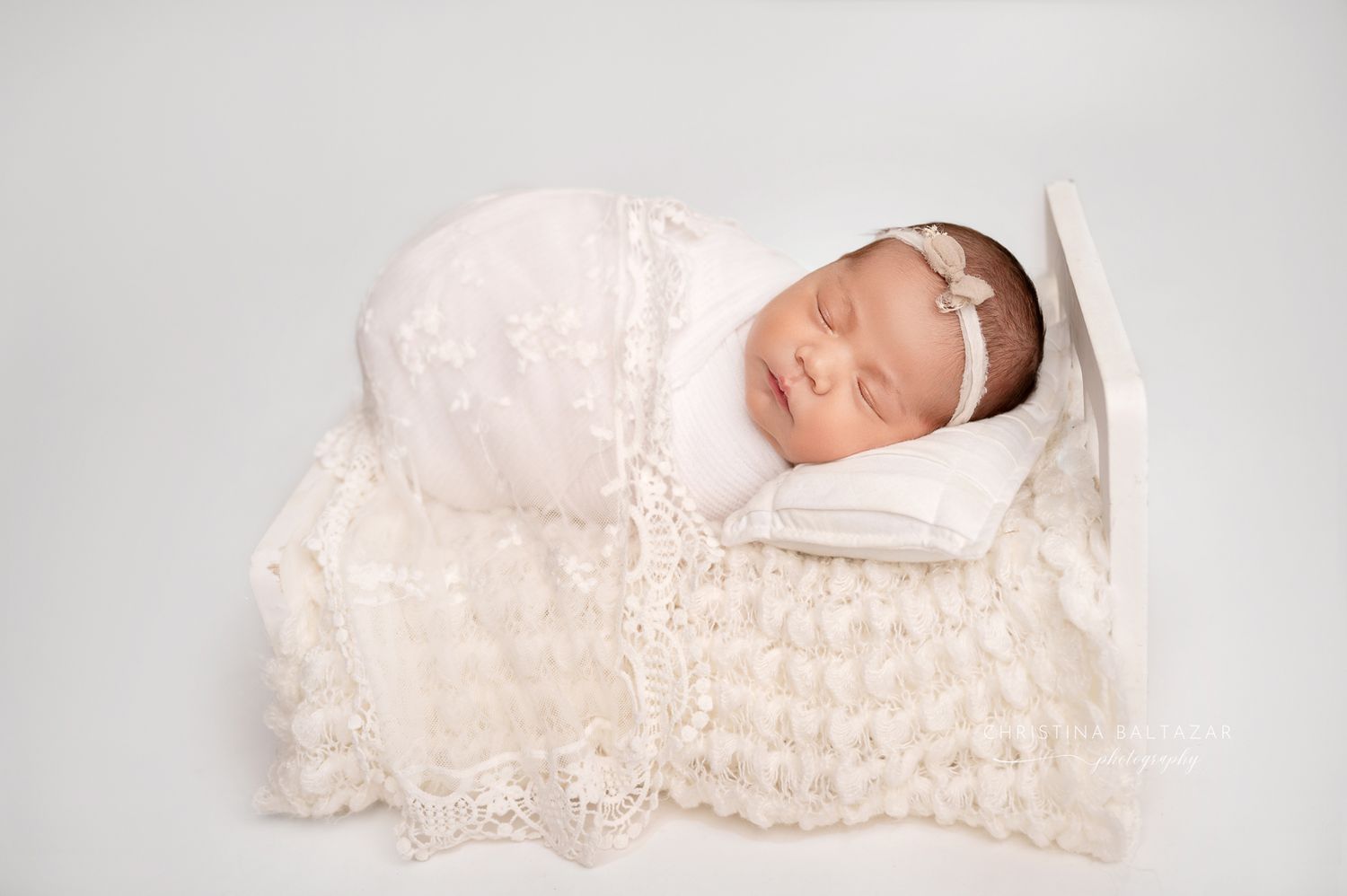 A sleeping newborn wrapped in delicate white lace rests peacefully on a soft blanket. Fresno Newborn Photographer