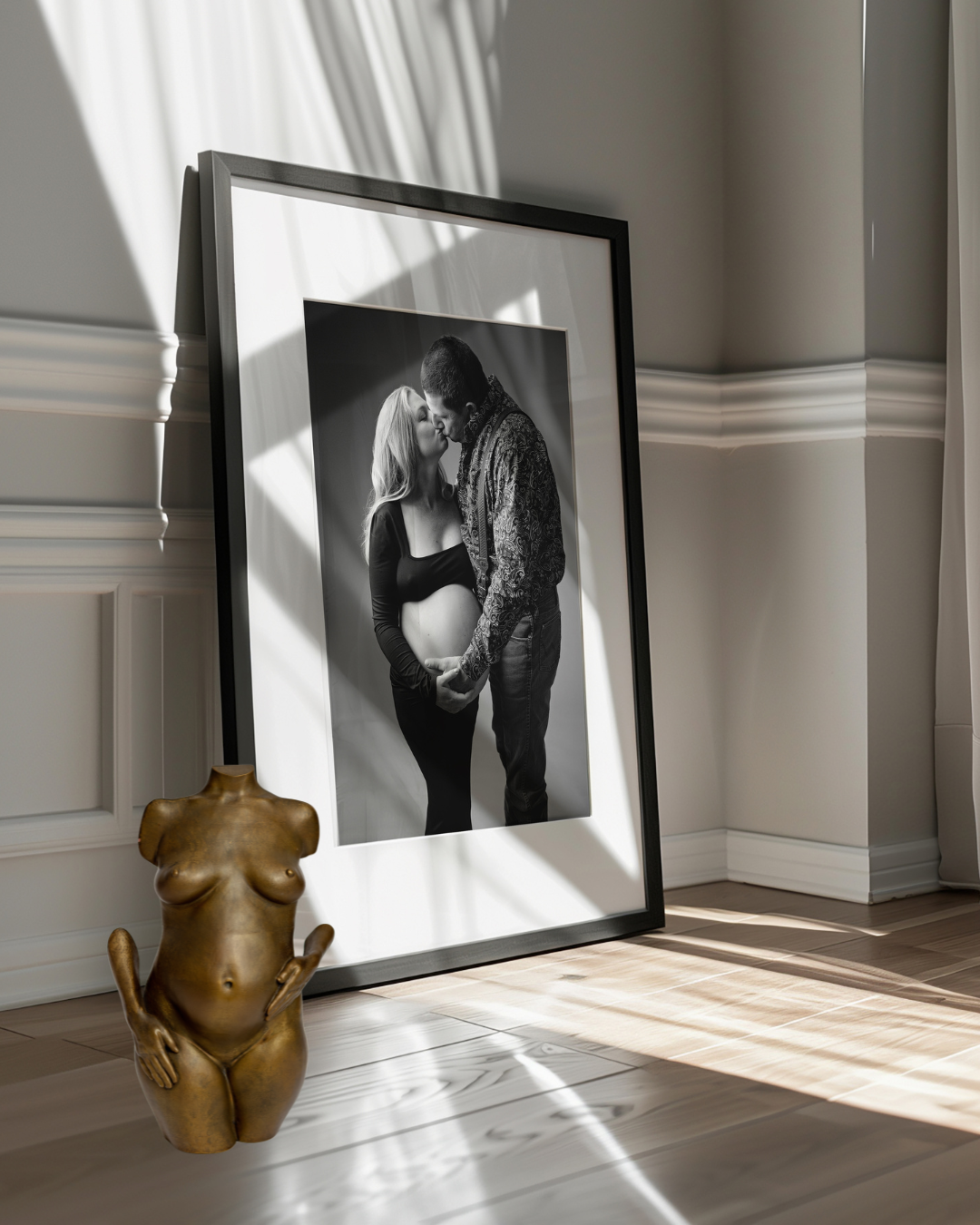 Black and white maternity photo in a black frame leaning against a wall, beside a gold pregnancy sculpture in Lemoore, CA