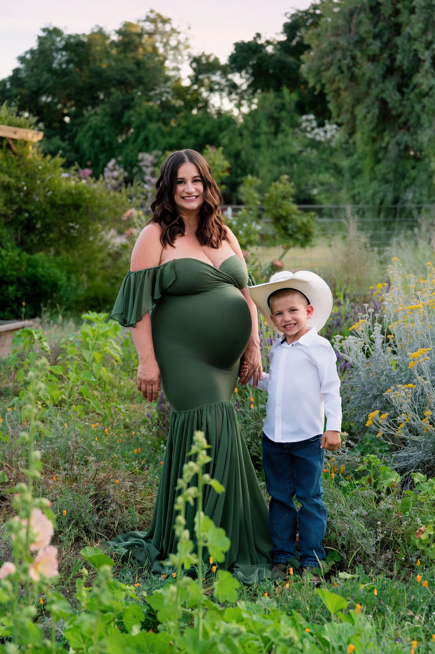 A maternity photoshoot in a wildflower garden features a green dress and natural scenery.