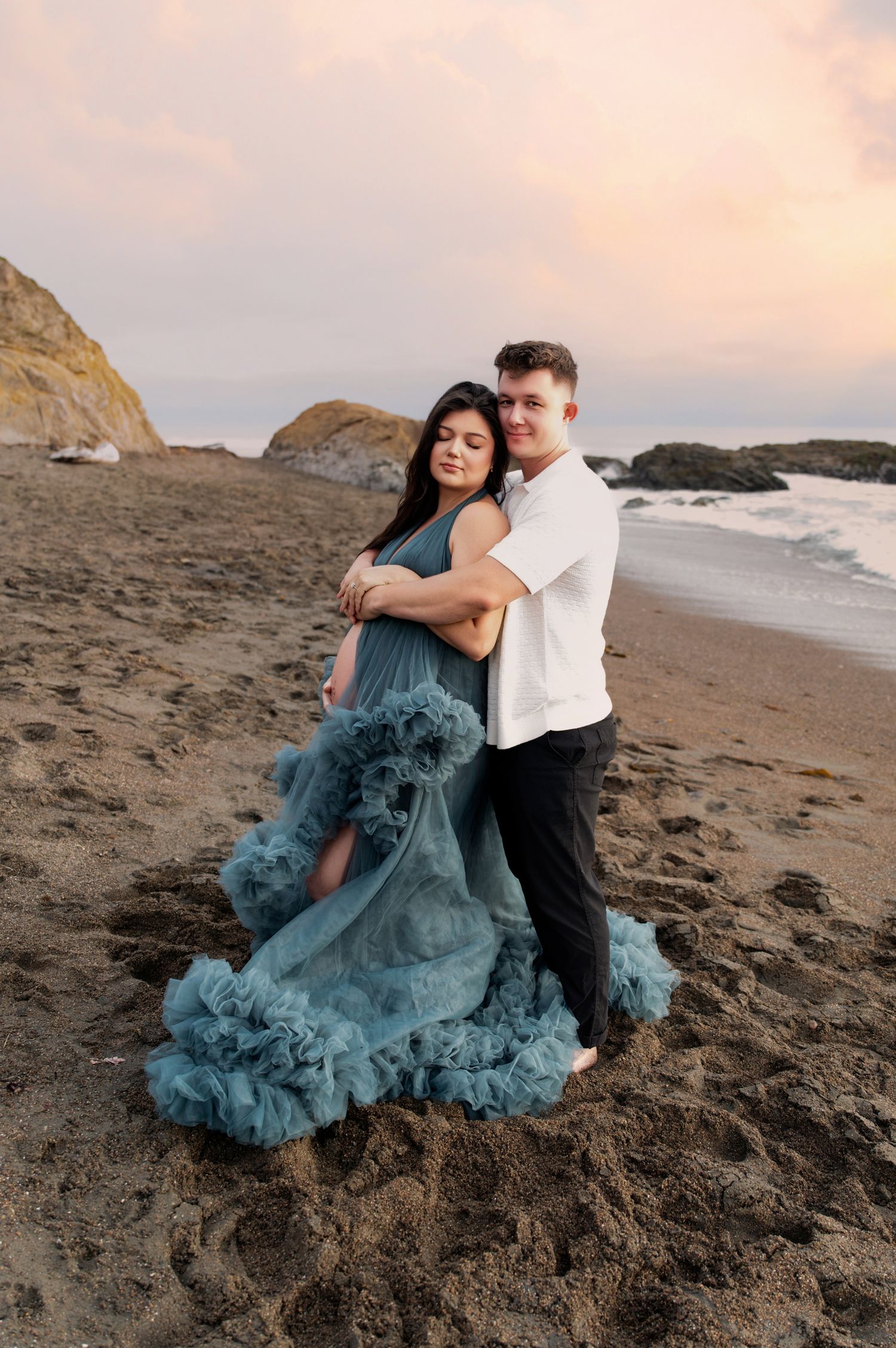 Beach maternity shoot with dramatic teal ruffled dress at sunset.