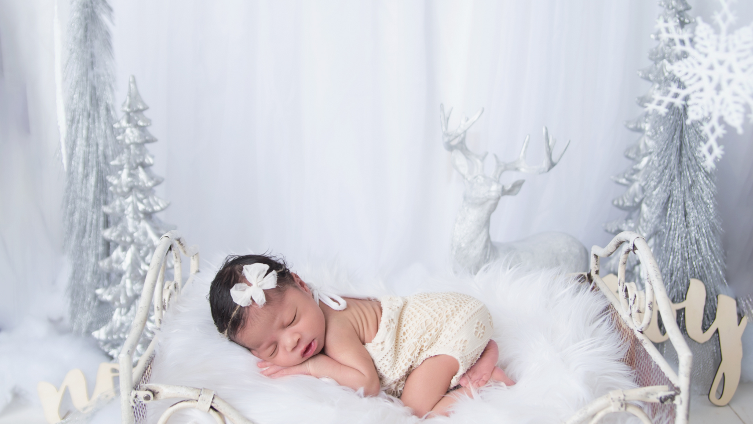 Sleeping newborn on white blanket in winter wonderland setting with snowflakes and ethereal lighting.