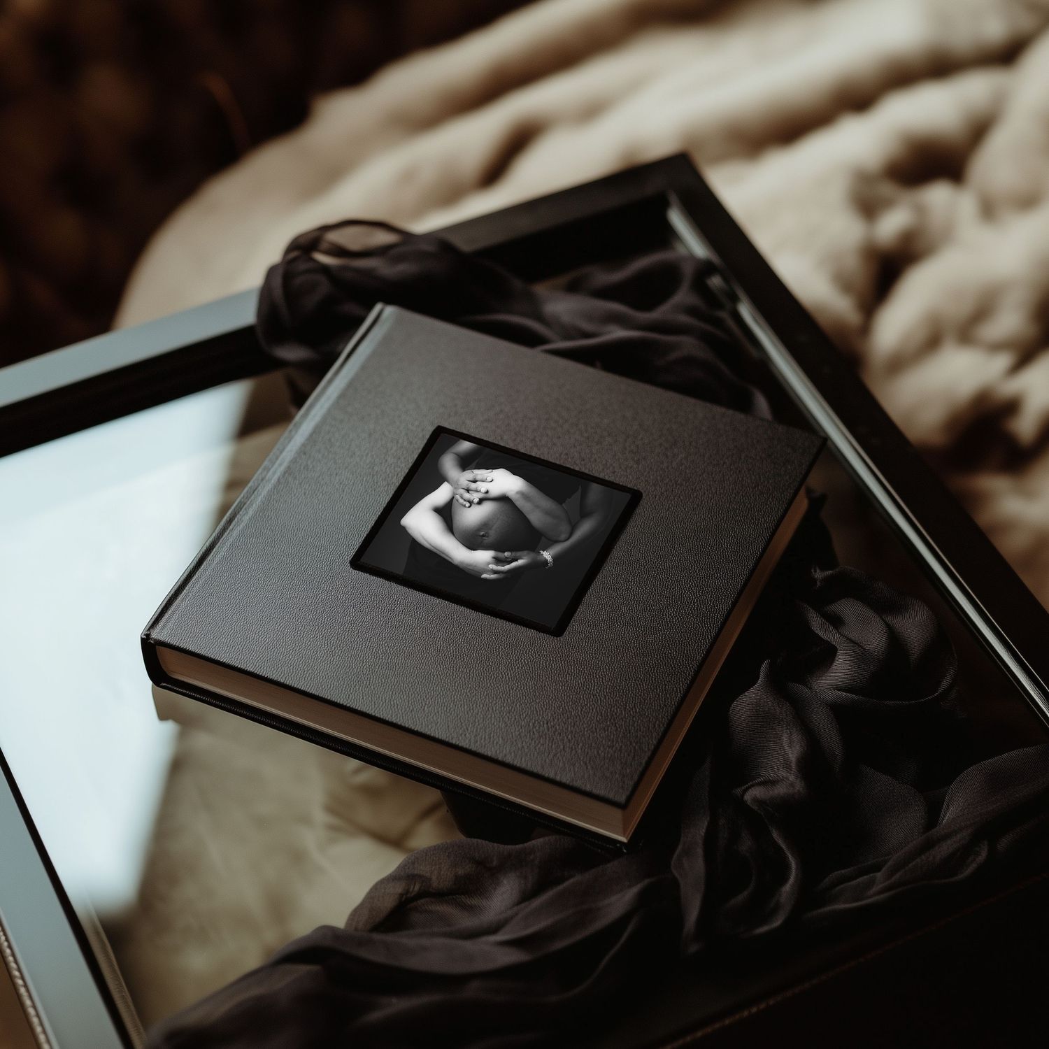 Black maternity photo album with sonogram image on cover rests on dark fabric surface. Hanford Maternity Photographer