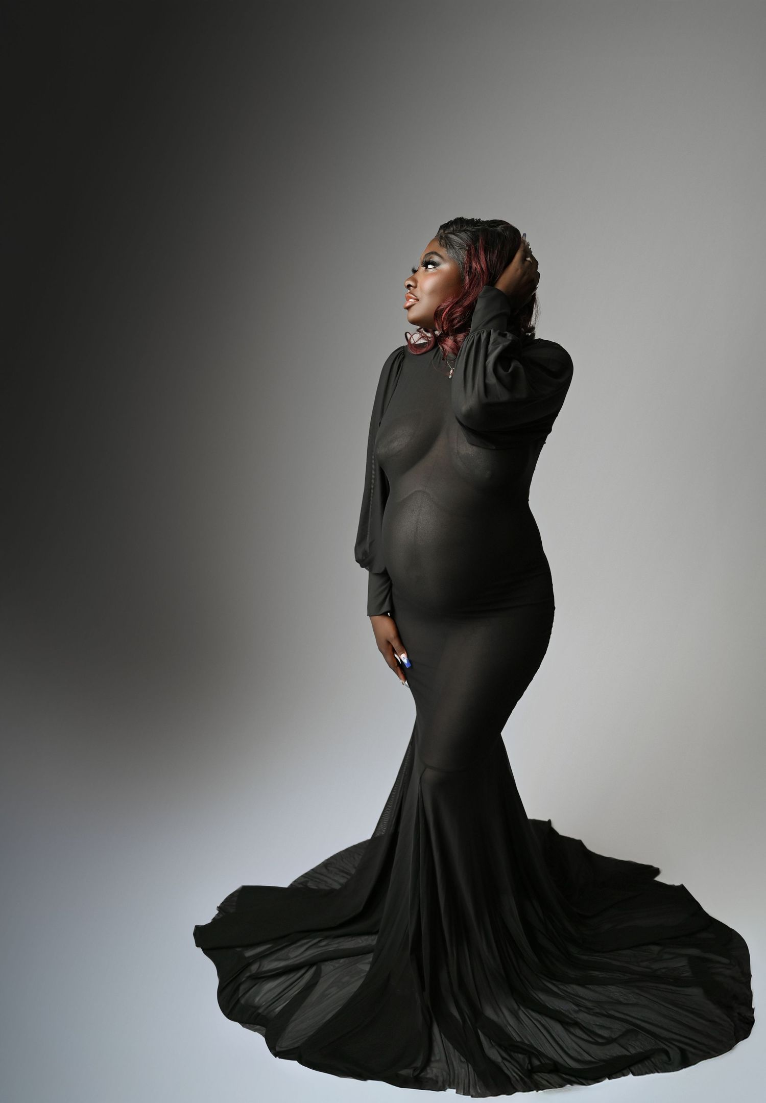 Dramatic maternity portrait in a flowing black mermaid gown against a gray backdrop.