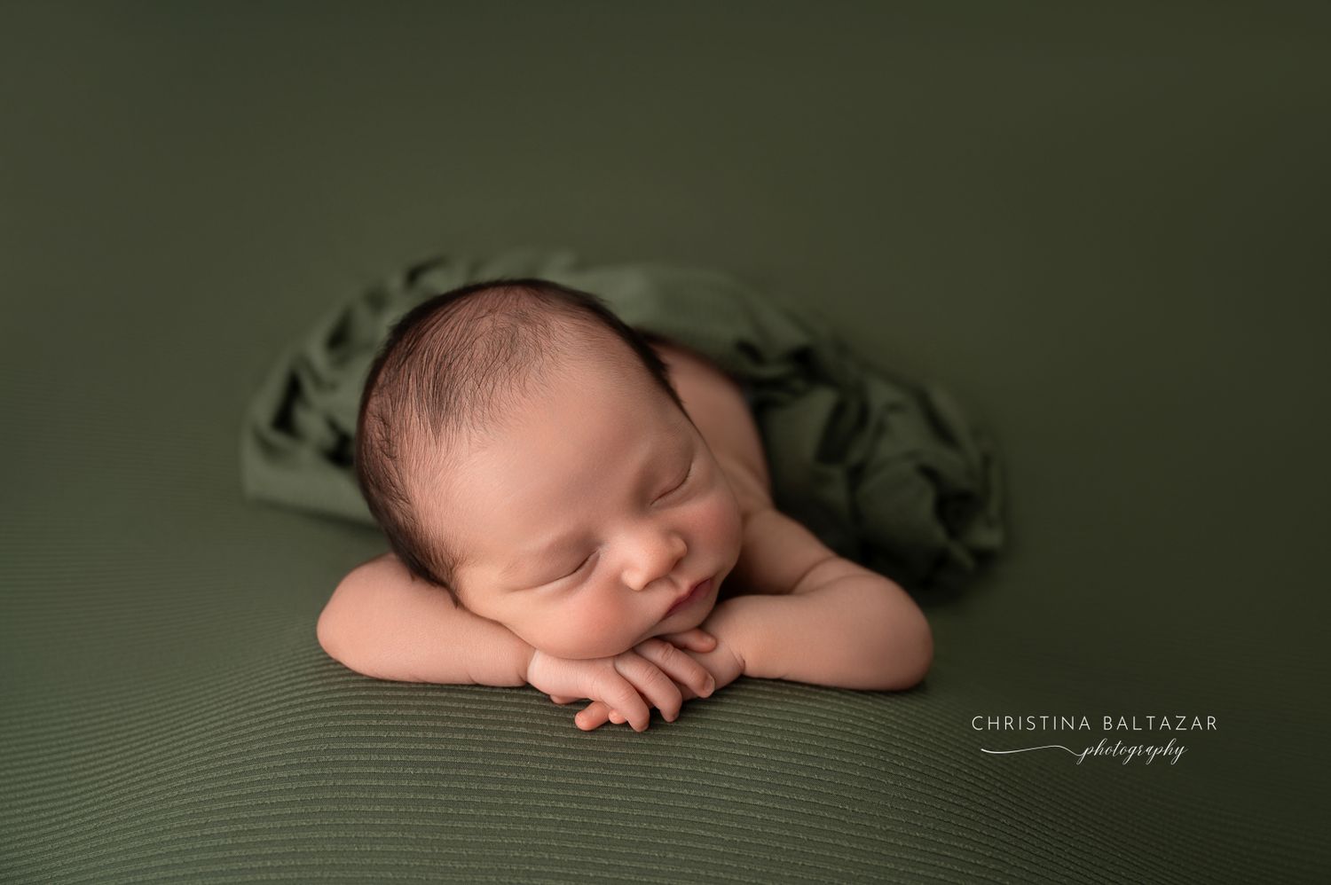 Sleeping newborn lying on dark green blanket with arms folded under head in studio portrait. Fresno Newborn Photographer
