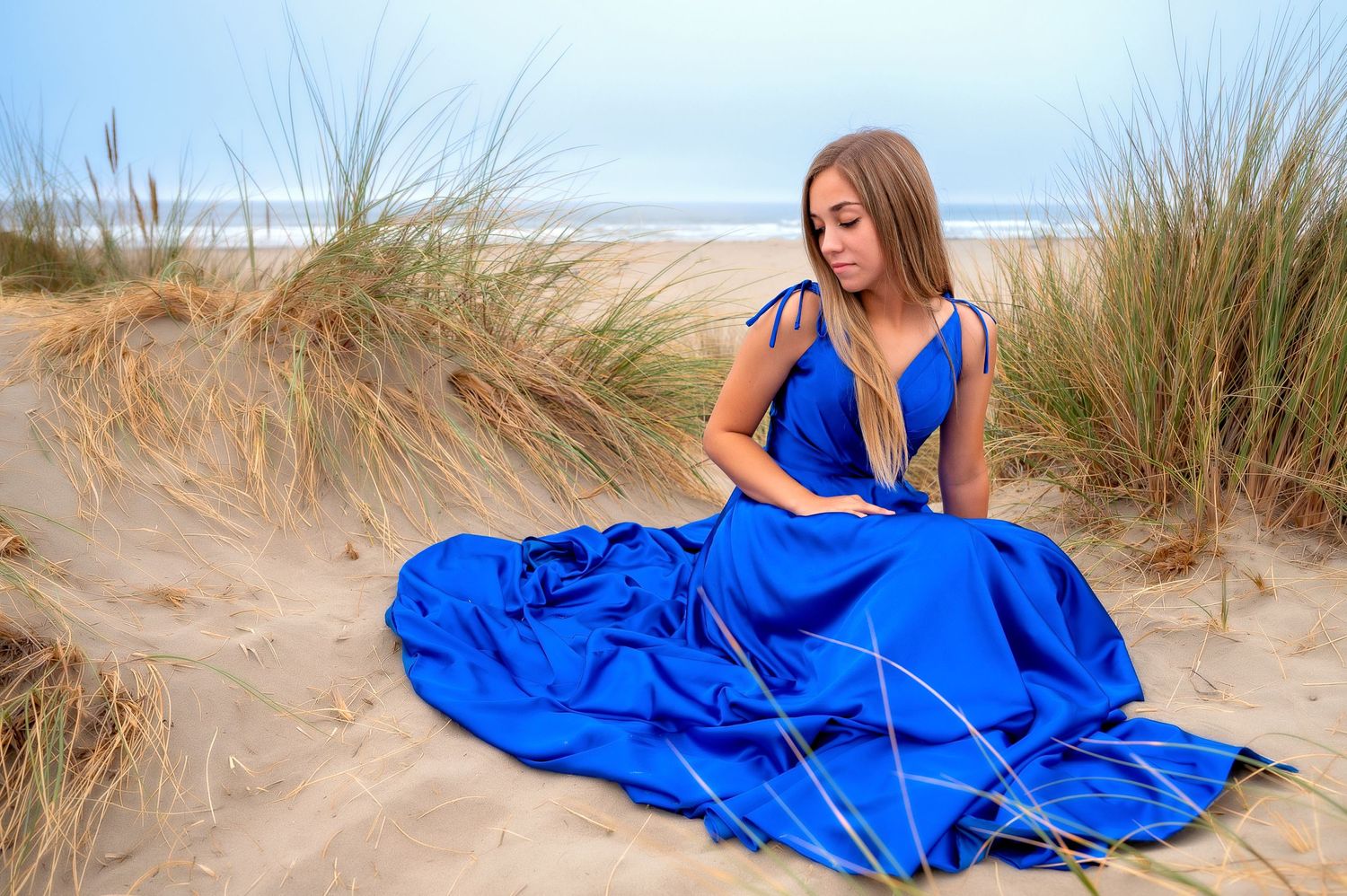 Elegant blue dress spread across sandy beach dunes with coastal grasses.