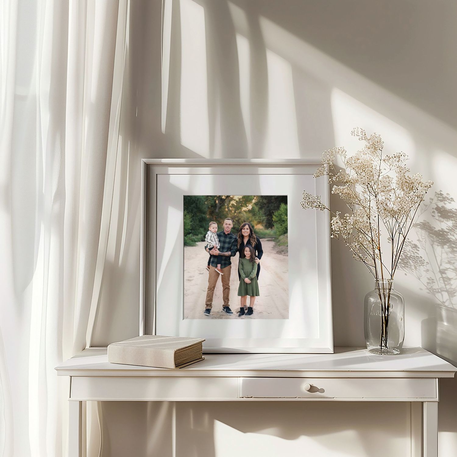 White floating shelves displaying family photos and dried flowers create a minimalist gallery wall in bright sunlight.