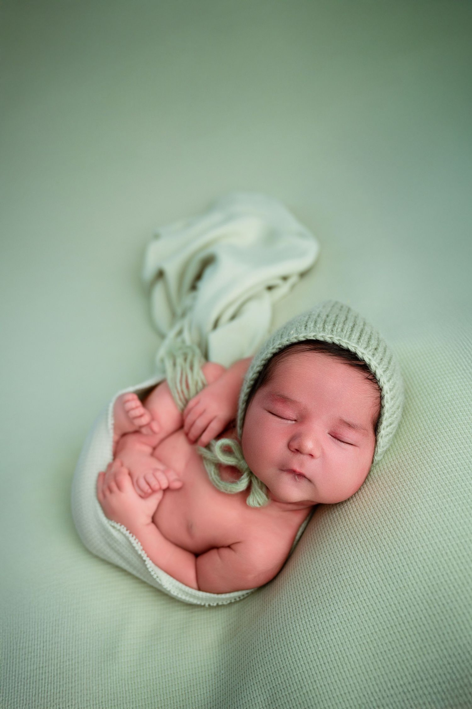 Sleeping newborn wearing white knit hat on mint green backdrop.