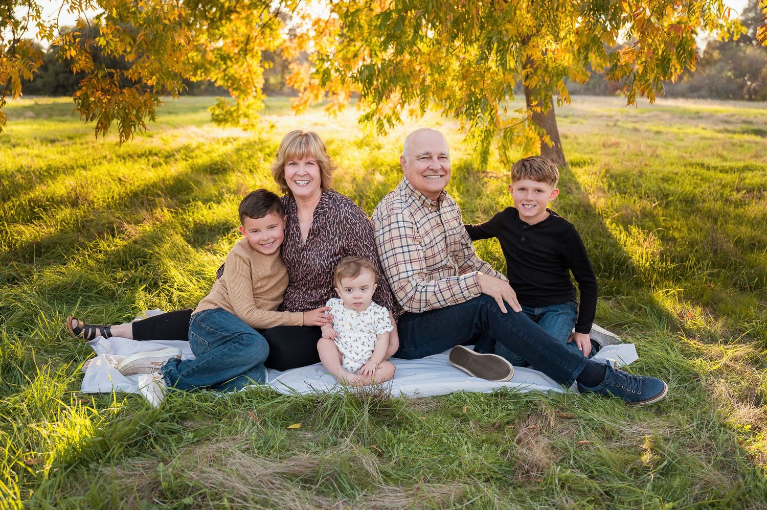 Family group lounges together on white blanket during outdoor autumn photoshoot. Hanford Family Photographer