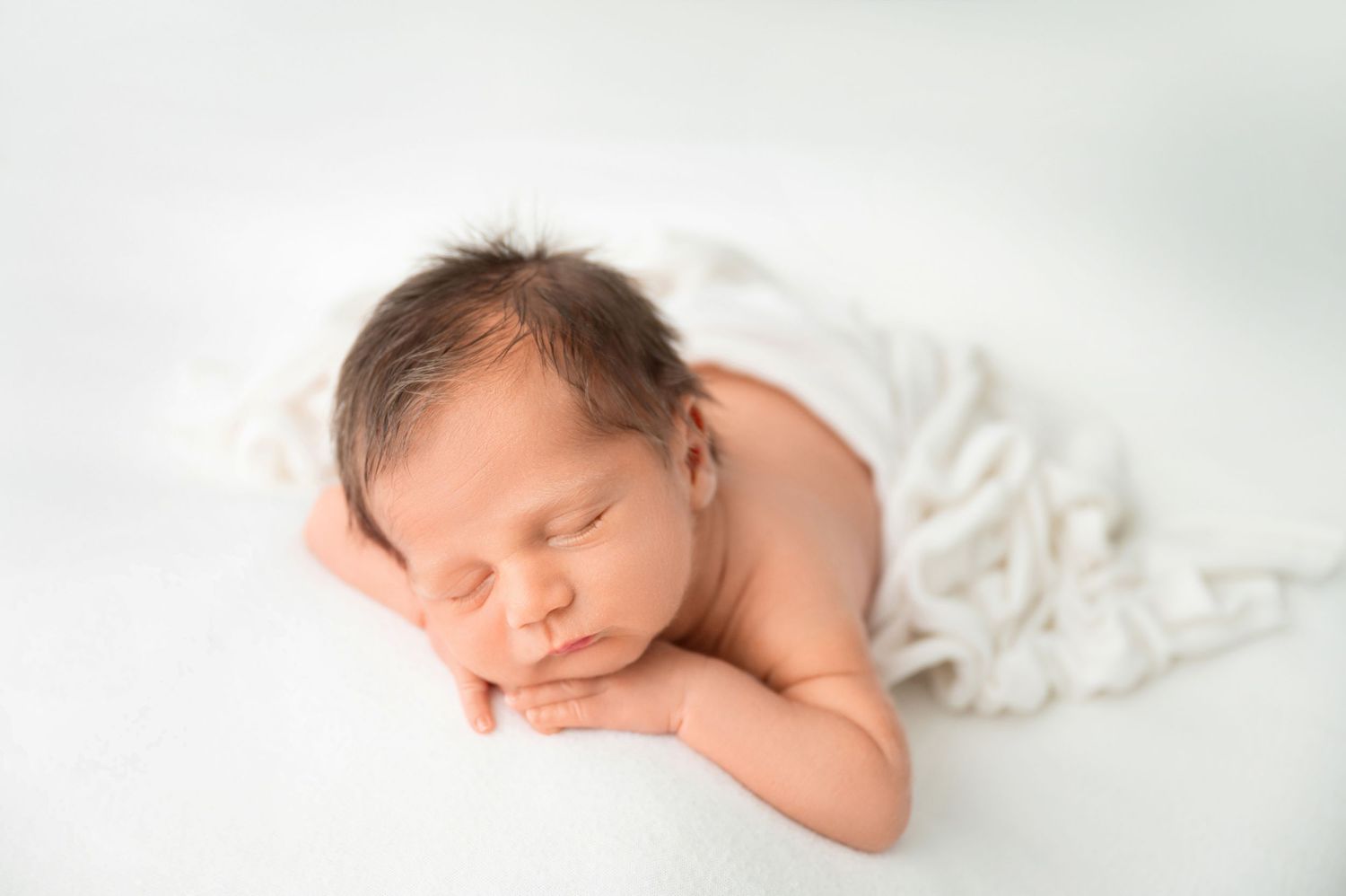 Serene newborn portrait with white blanket against light background.
