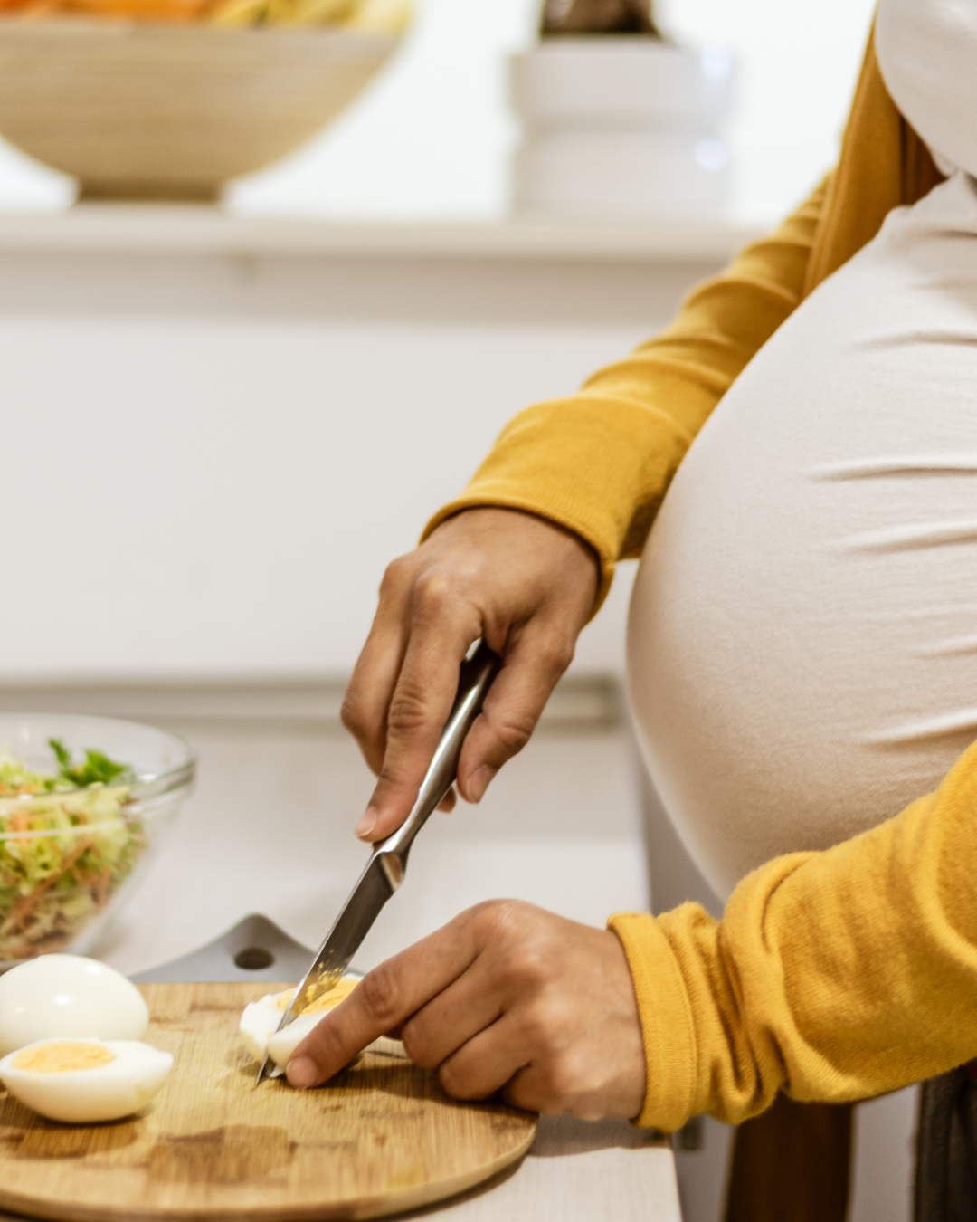 Woman in yellow sweater slices an onion on wooden cutting board while preparing a healthy meal.