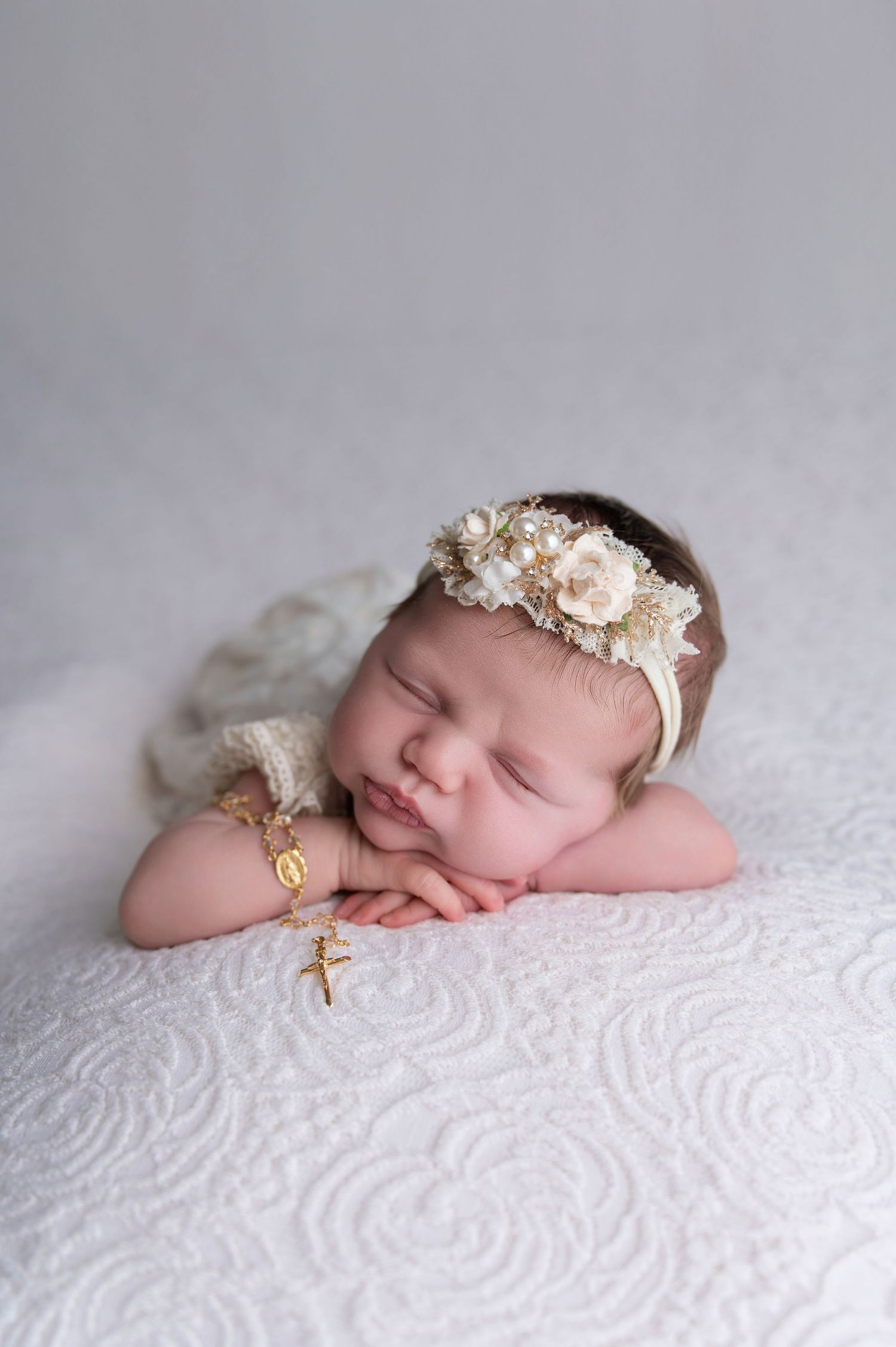 Sleeping newborn baby wearing delicate floral headband on textured white blanket.