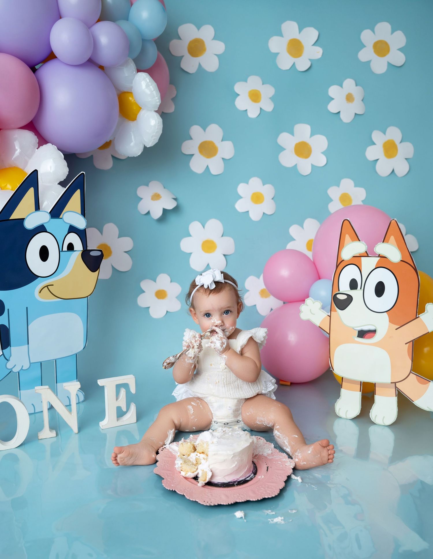 First birthday cake smash setup with pastel balloons, daisies and cartoon decorations.