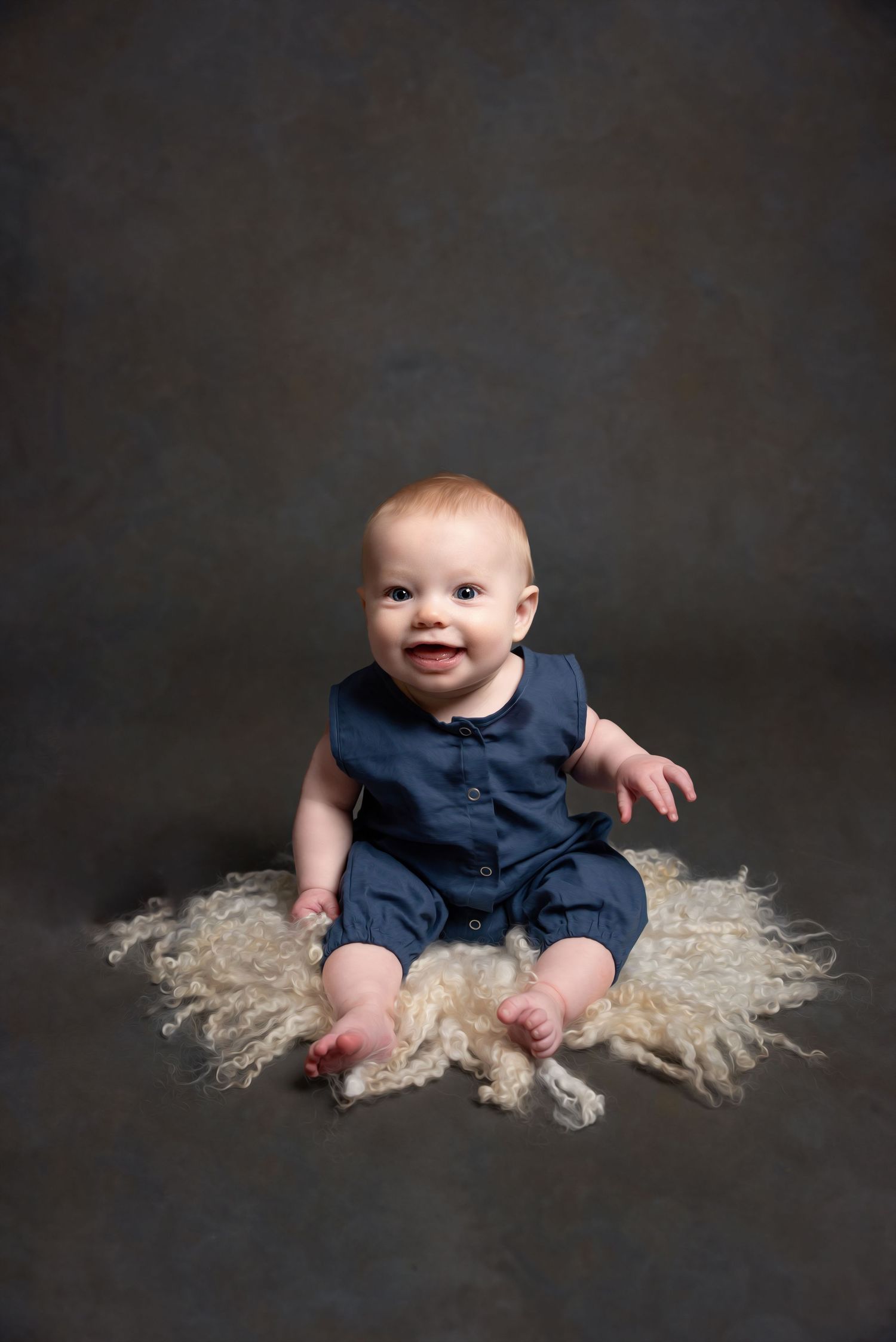 Baby in navy outfit photographed on textured fur rug against dark background.