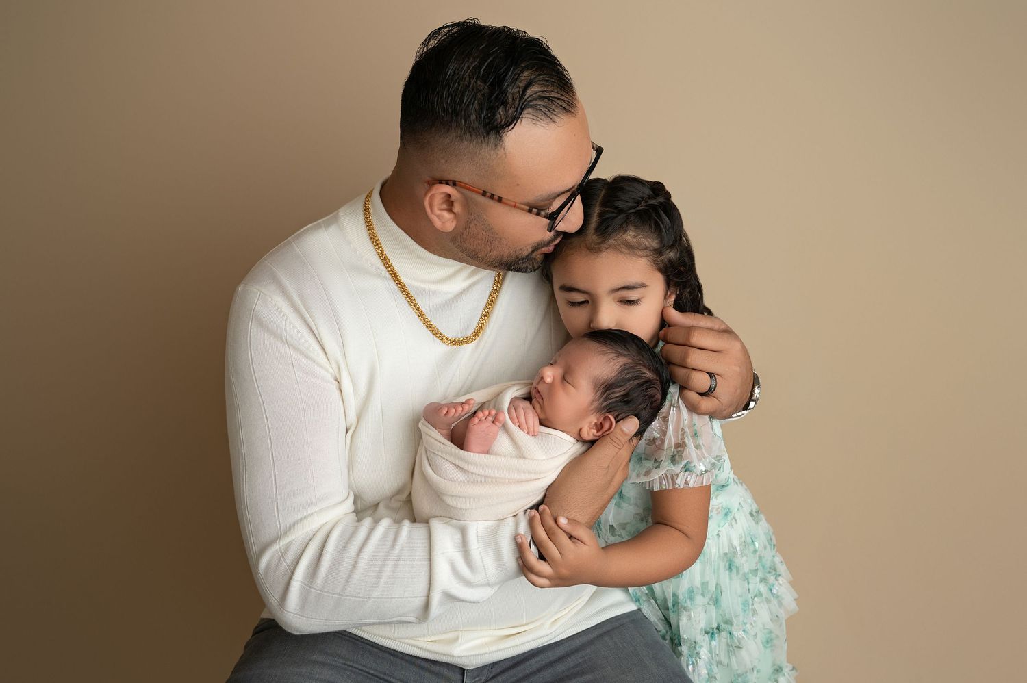 Emotional newborn photo session with parents in white and mint green outfits against beige background.