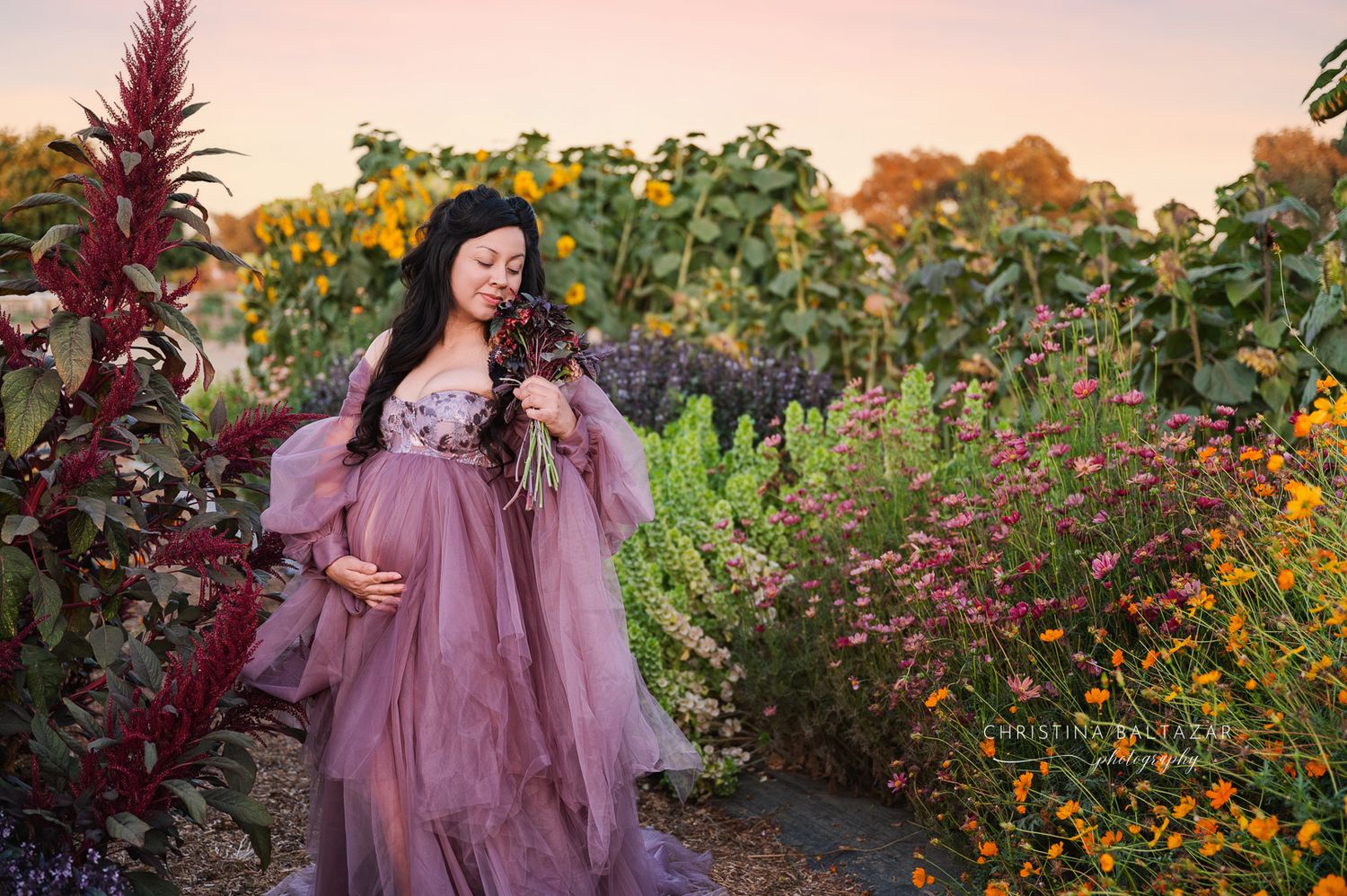 A dreamy scene in a garden with sunflowers and wildflowers featuring a flowing mauve dress among vibrant blooms. Fresno Maternity Photograph