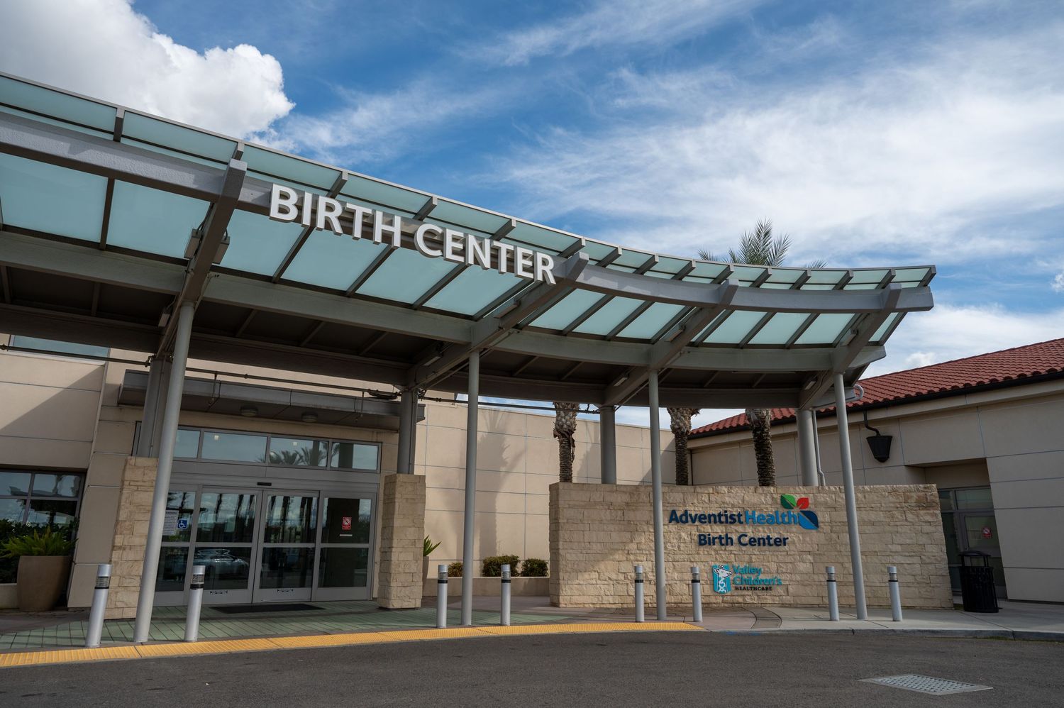 Modern birth center entrance with glass panels and covered walkway under blue sky.
