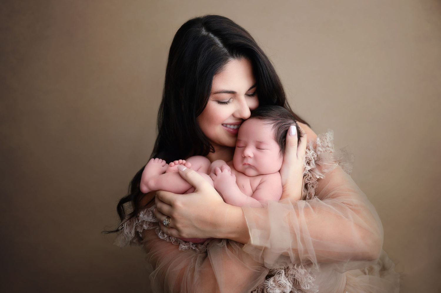 A tender moment captured in soft lighting as a newborn sleeps peacefully in a gentle embrace against sheer fabric. Fresno Newborn Photos