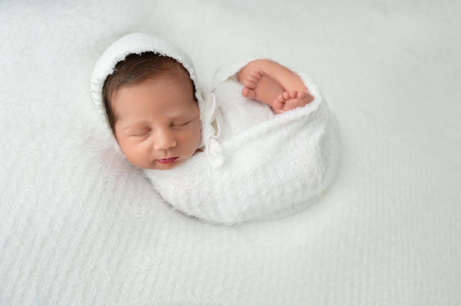 Sleeping newborn baby swaddled in soft white wrap against light background.