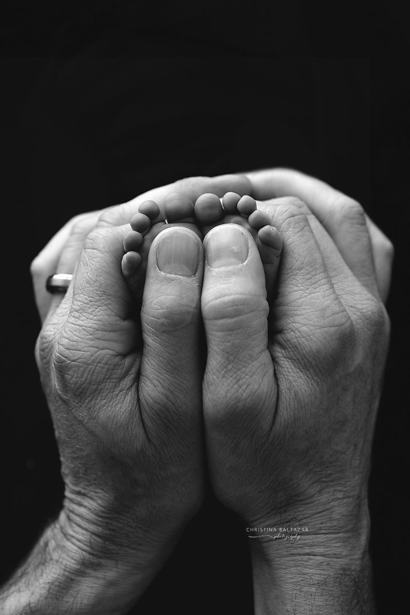 Intimate black and white photo of tiny baby feet cradled in adult hands.