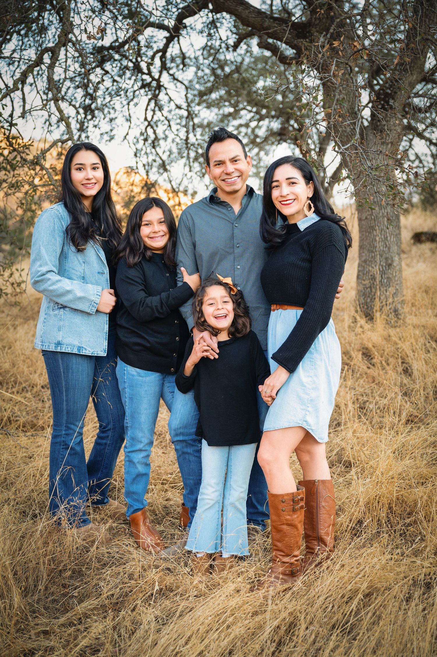 Group photo session in tall grass with oak trees during golden hour showing casual coordinated outfits. Hanford Family Photographer