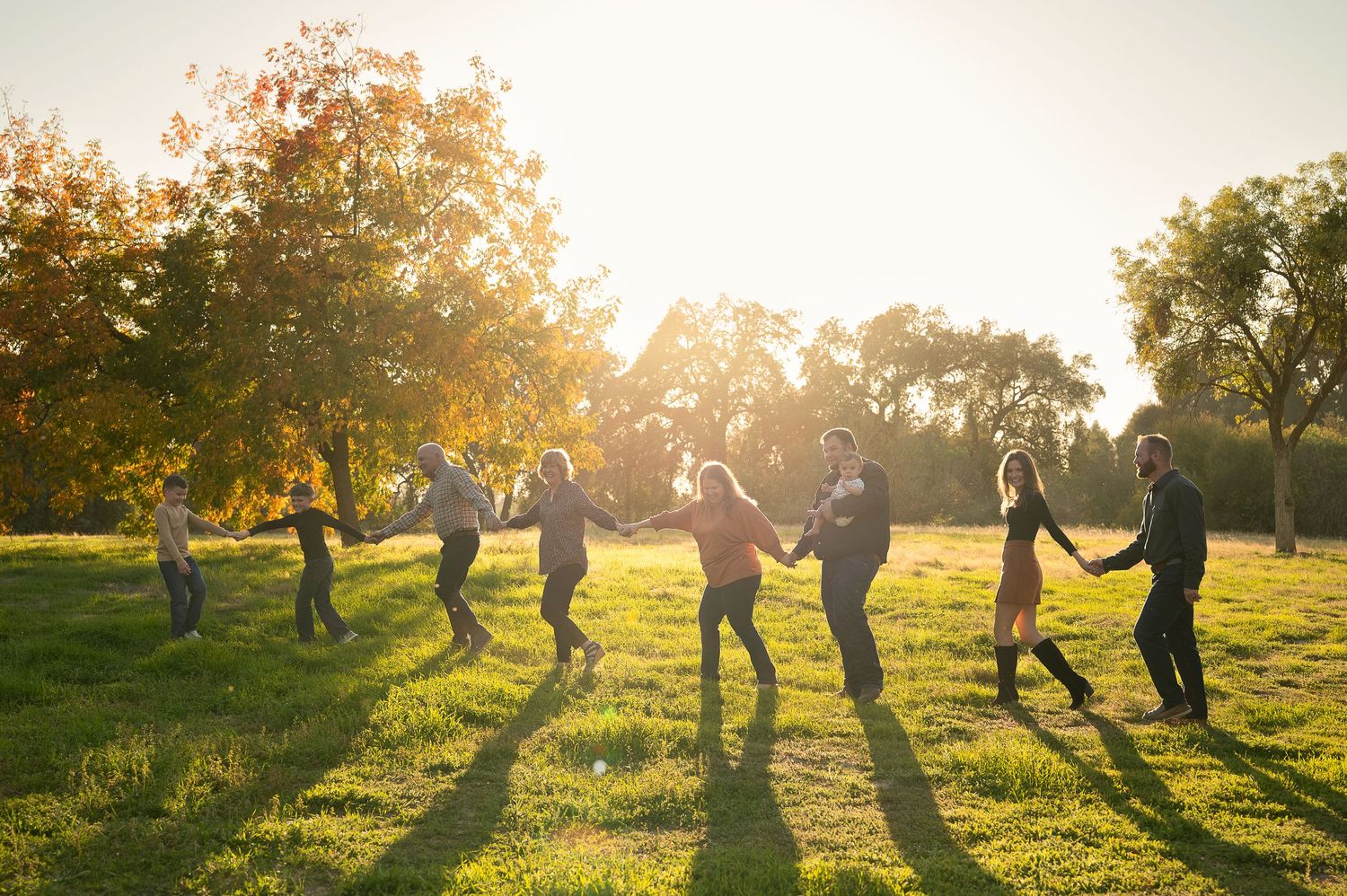 Silhouettes of family members playing and jumping in golden sunlight during sunset photo session. Hanford Family Photographer