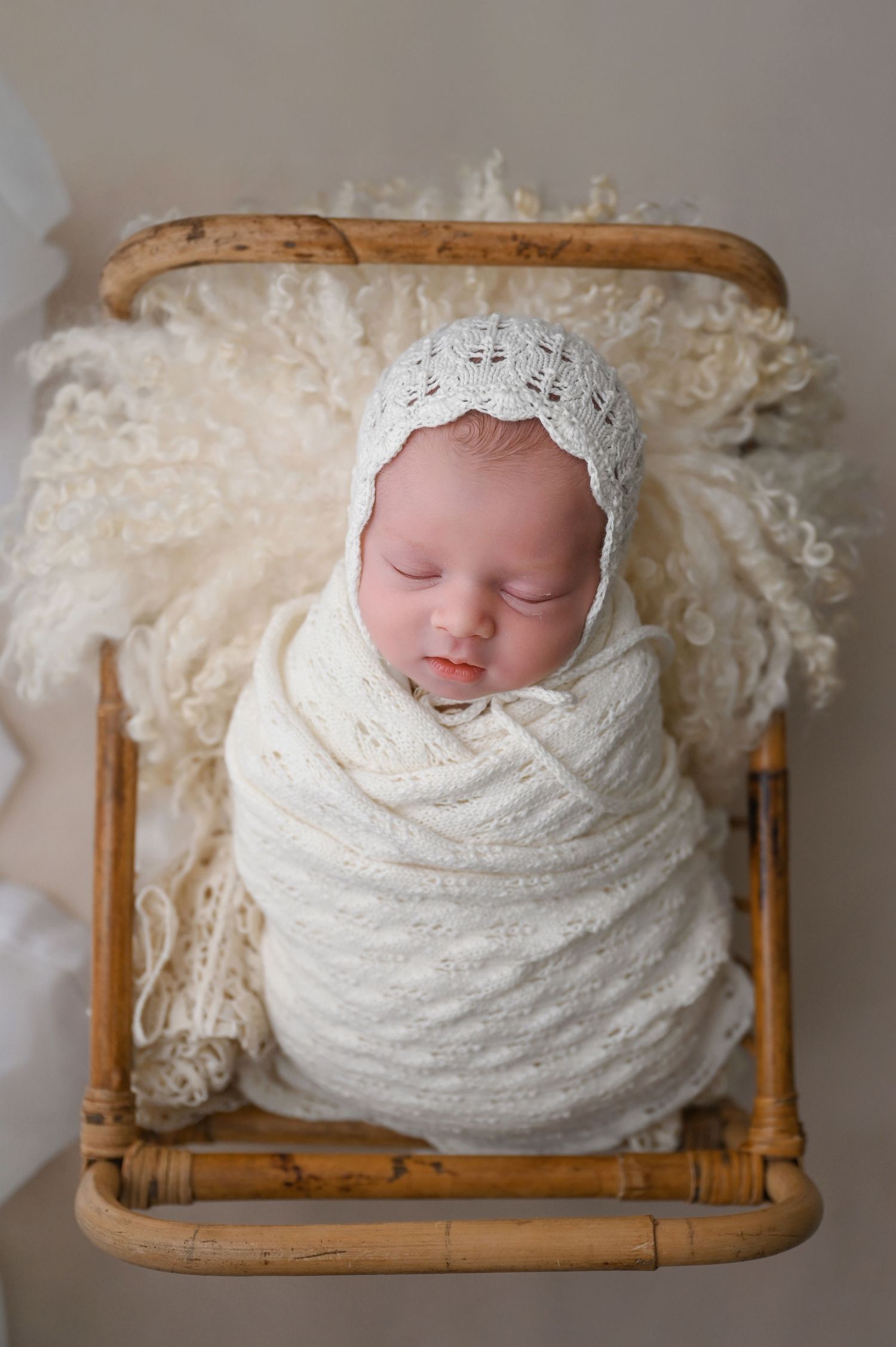 Newborn baby wrapped in cream lace swaddle resting in vintage wooden basket.
